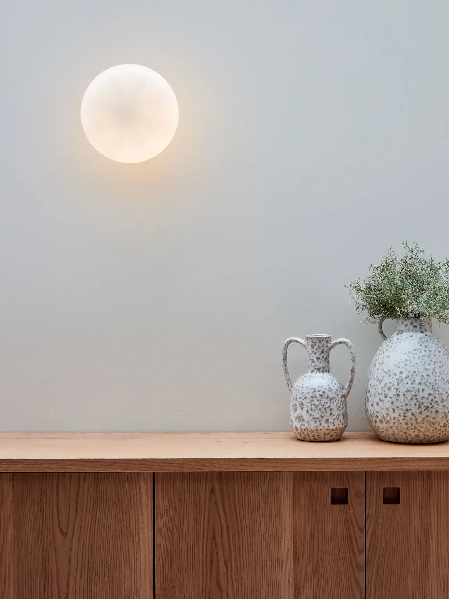 Pluck's Elm wood shallow cabinets with vases and a moon like light.