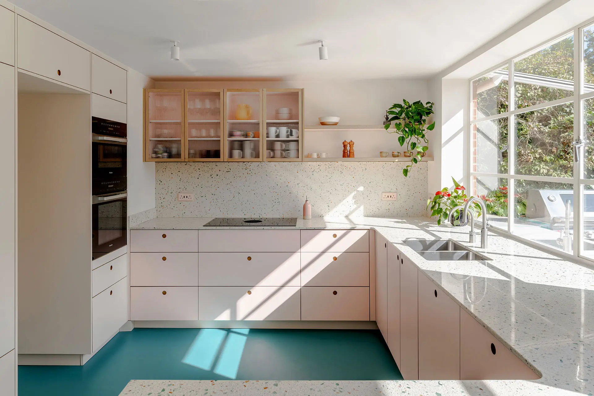 Pastel kitchen with pale pink and soft beige cabinets including a peninsula, all topped with terrazzo, surrounded by a bold blue floor.