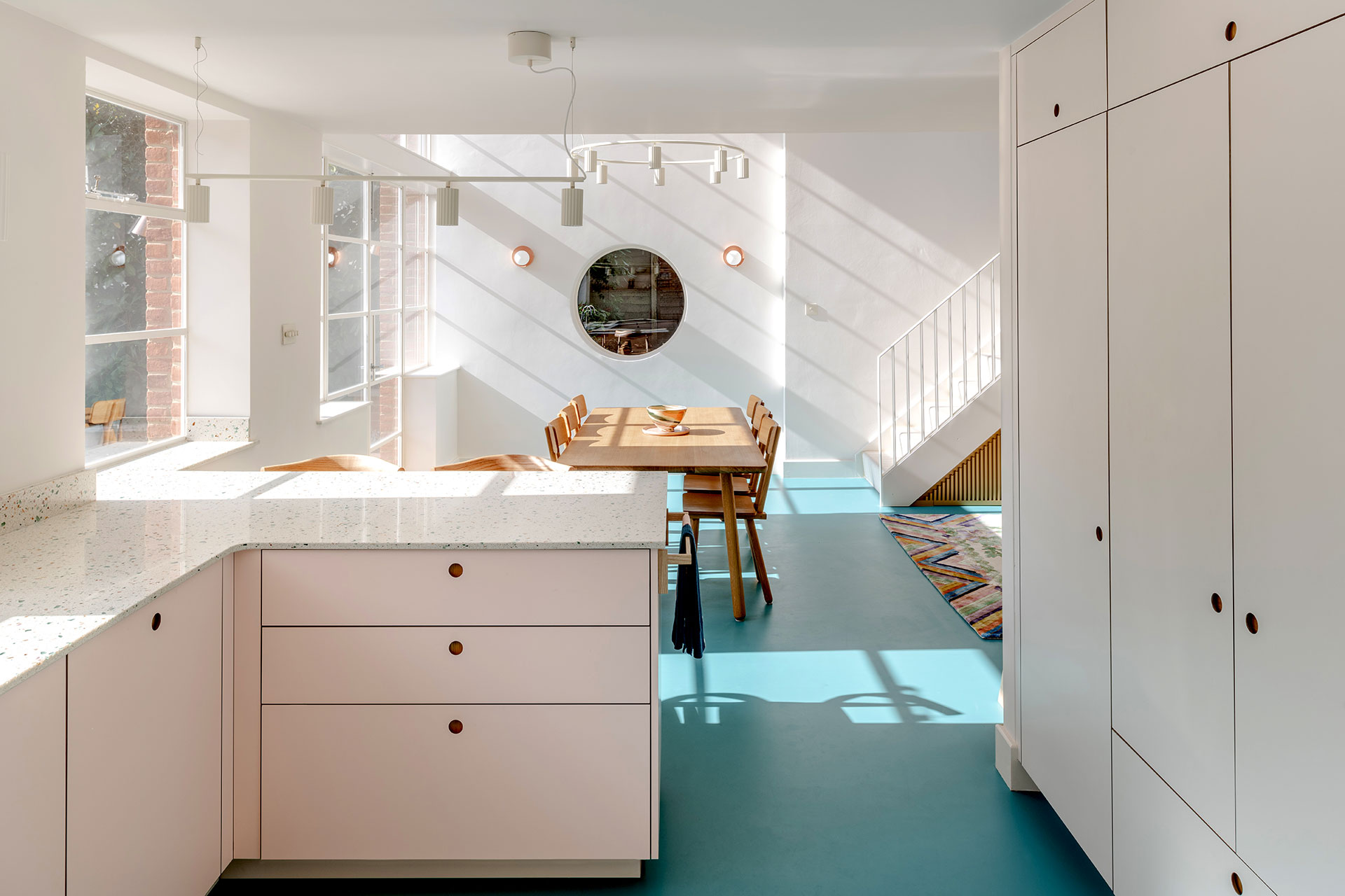 Pastel pink and beige Pluck cabinetry in an open plan space with a bright blue floor.