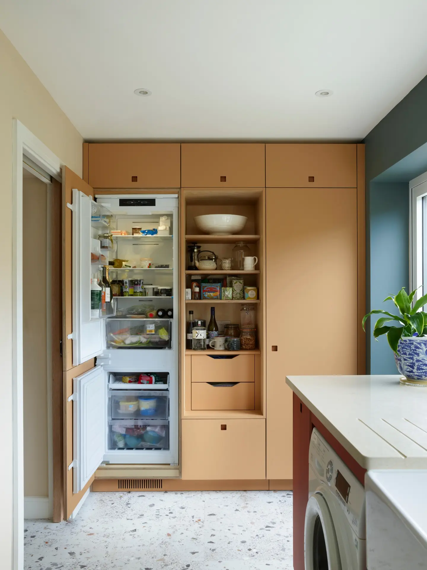Moody hues of a kitchen in Essex with orange and red two tone cabinetry and a navy blue wall.