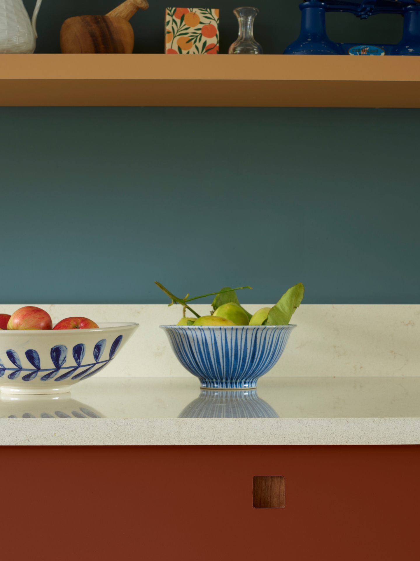 Moody hues of a kitchen in Essex with orange and red two tone cabinetry and a navy blue wall.
