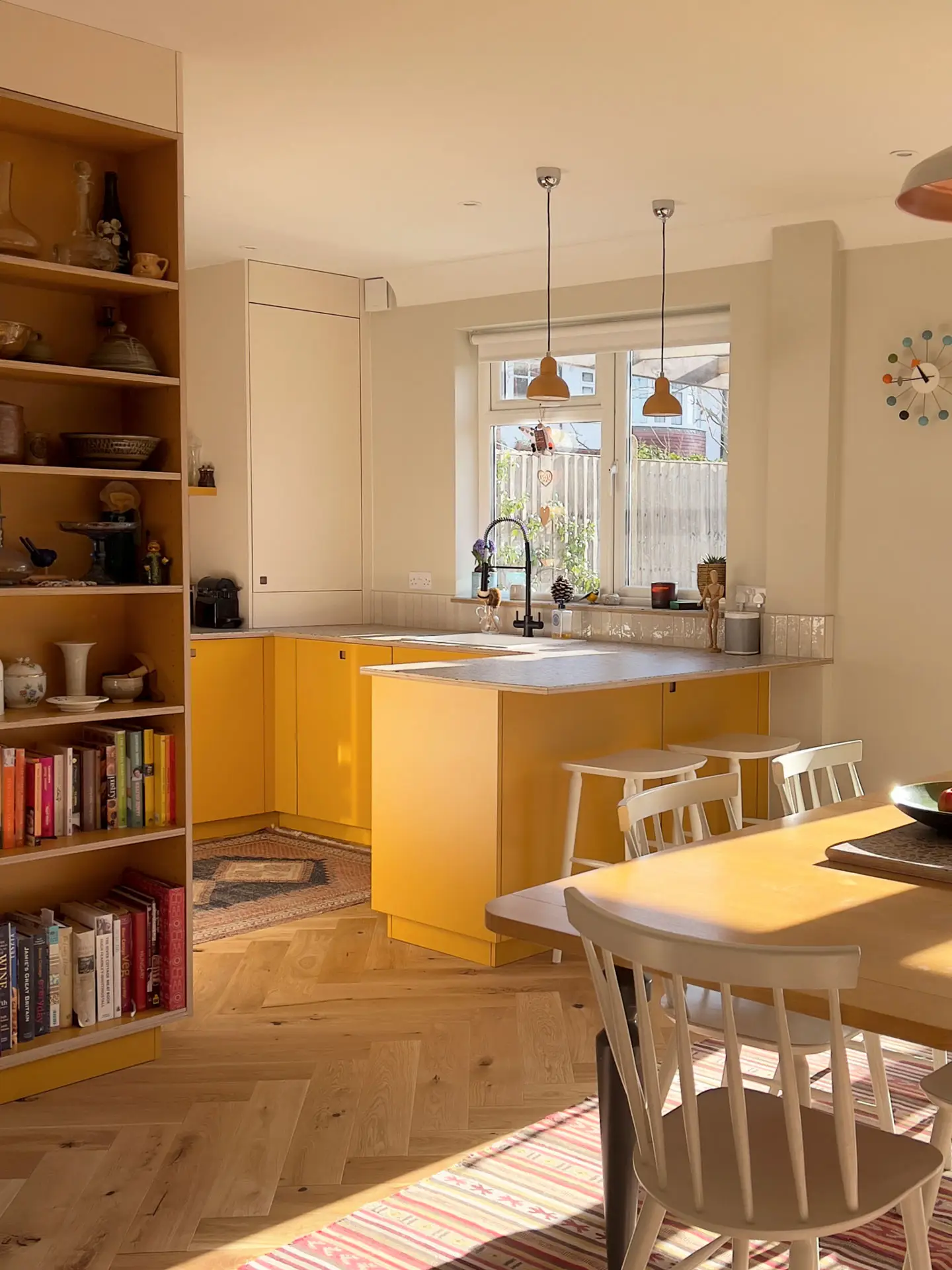 Small kitchen in South London with mustard yellow and pale beige cabinets including a peninsula, topped with a wood terrazzo surface.