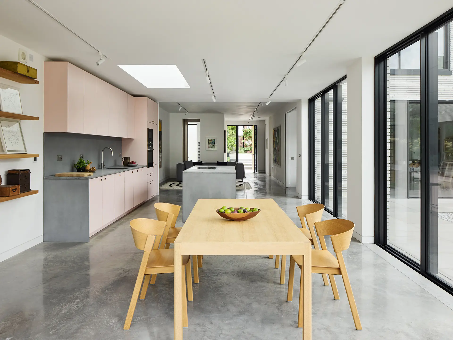 Two neighbouring homes with Pluck cabinetry including a wood and white kitchen and a pink kitchen, both with concrete.