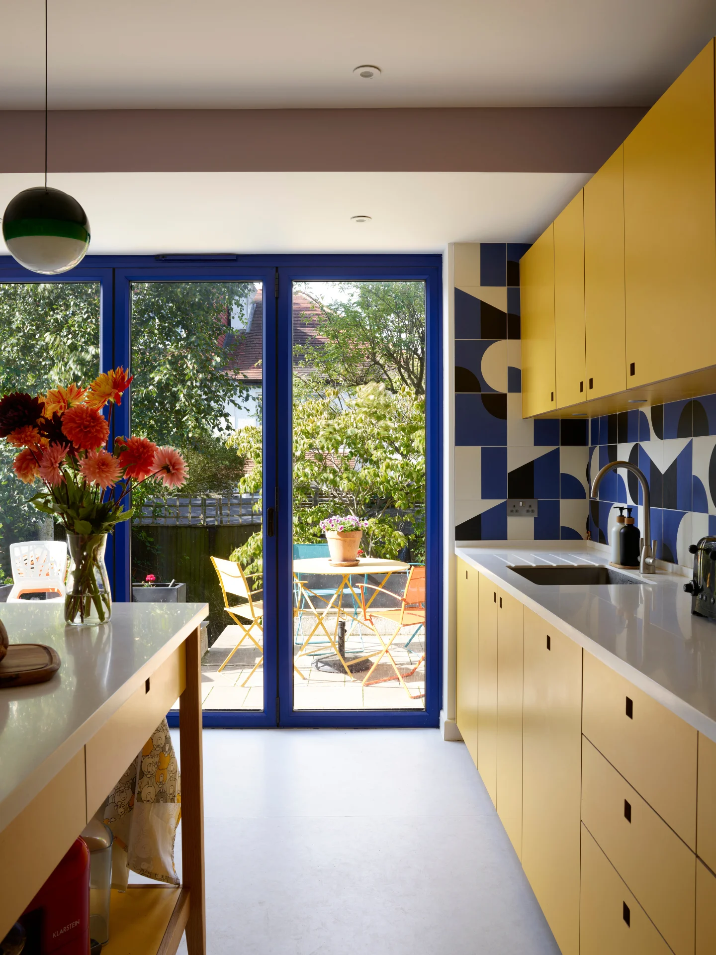 Bright sunshine yellow kitchen in Herne Hill with a freestanding prep table island and cobalt blue glazing and patterned tile splashback.