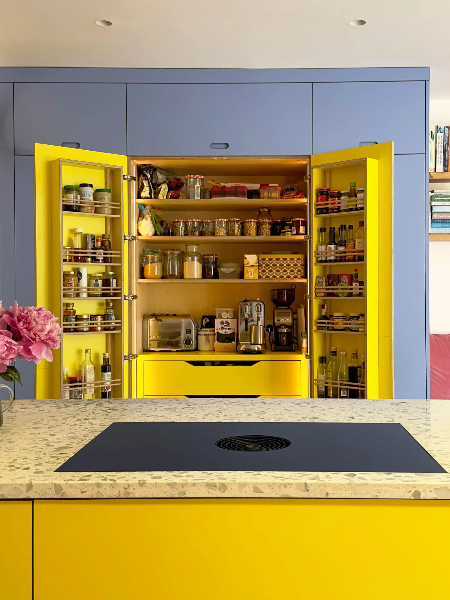 Larder cupboard in a Pluck kitchen with blue cabinets and yellow interior and a terrazzo topped island with a hob.