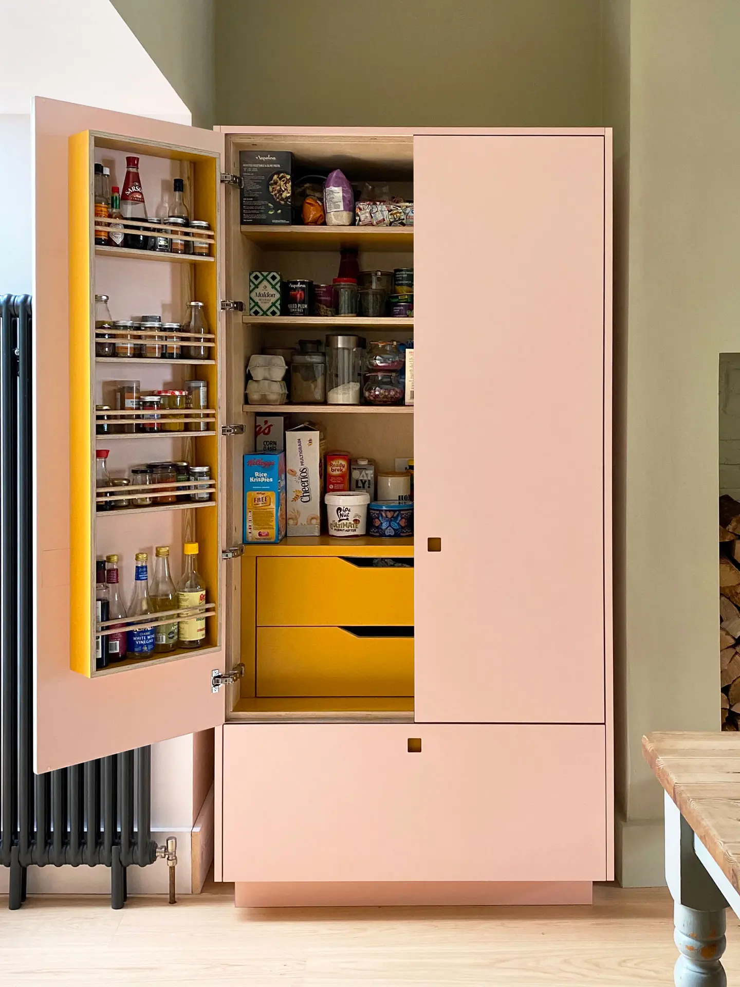 A freestanding Pluck larder with a pink exterior and mustard yellow interior in a family home.