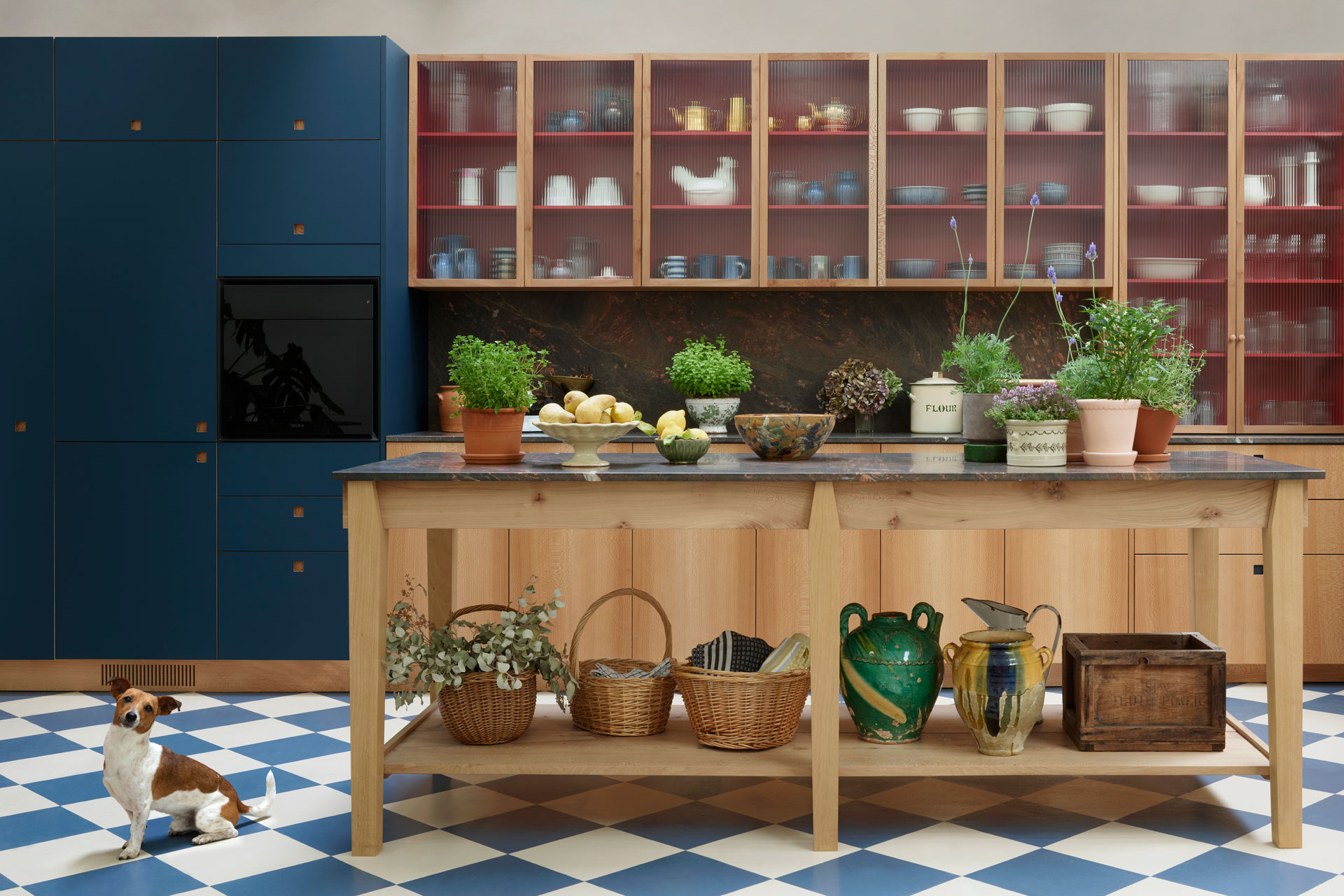 Kitchen showroom with London Plane, rich red and deep blue cupboards and a wooden work table with quartzite.
