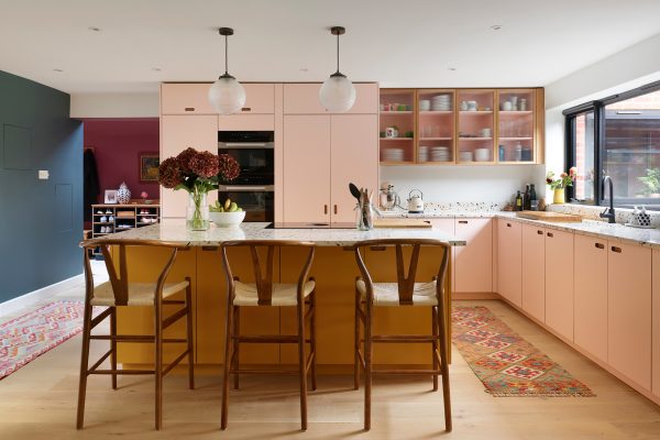 Colourful family kitchen in Hertfordshire including soft pink and mustard yellow Pluck cabinets, a large island and navy blue walls.