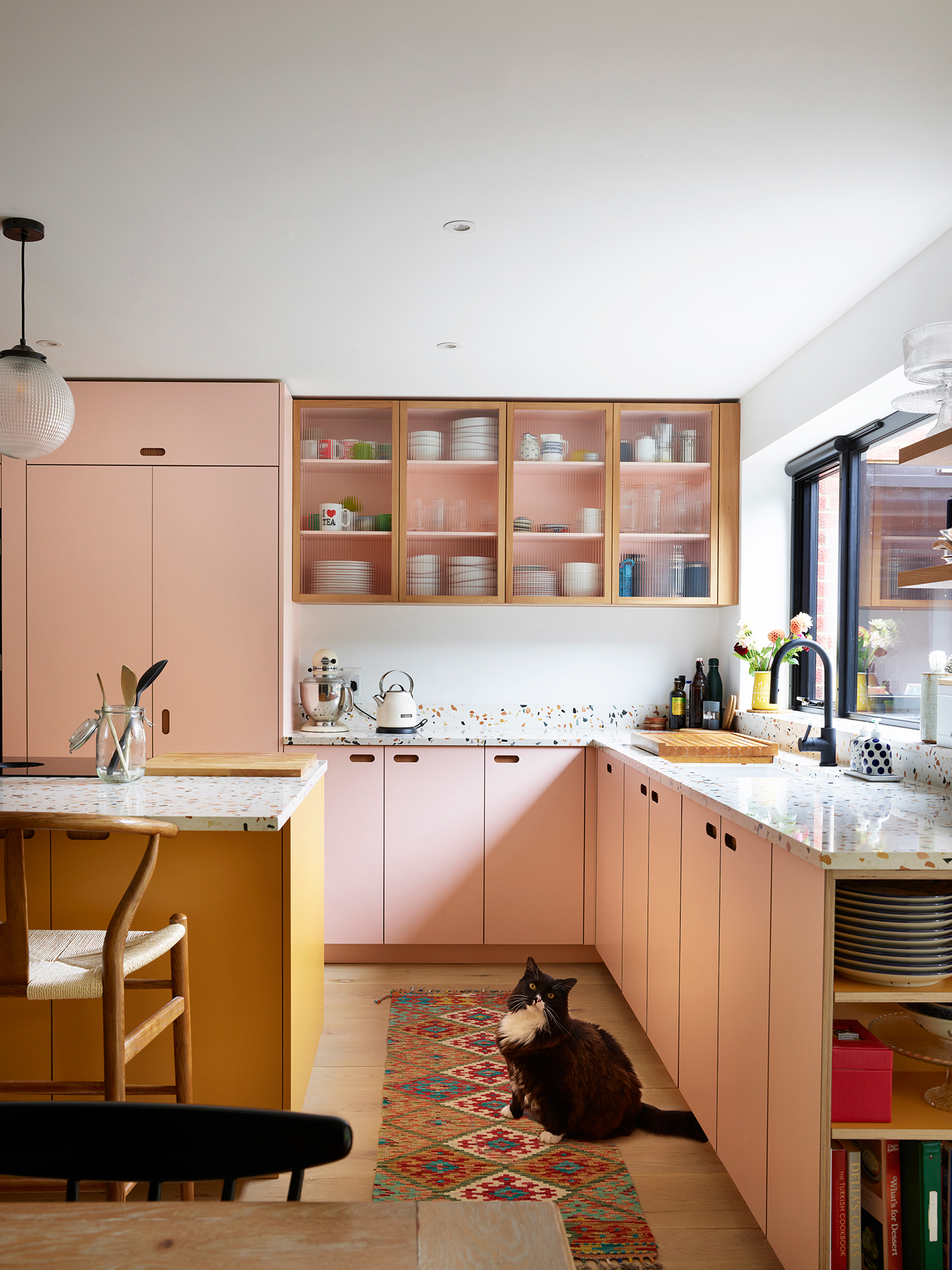 Colourful family kitchen in Hertfordshire including soft pink and mustard yellow Pluck cabinets, a large island and navy blue walls.