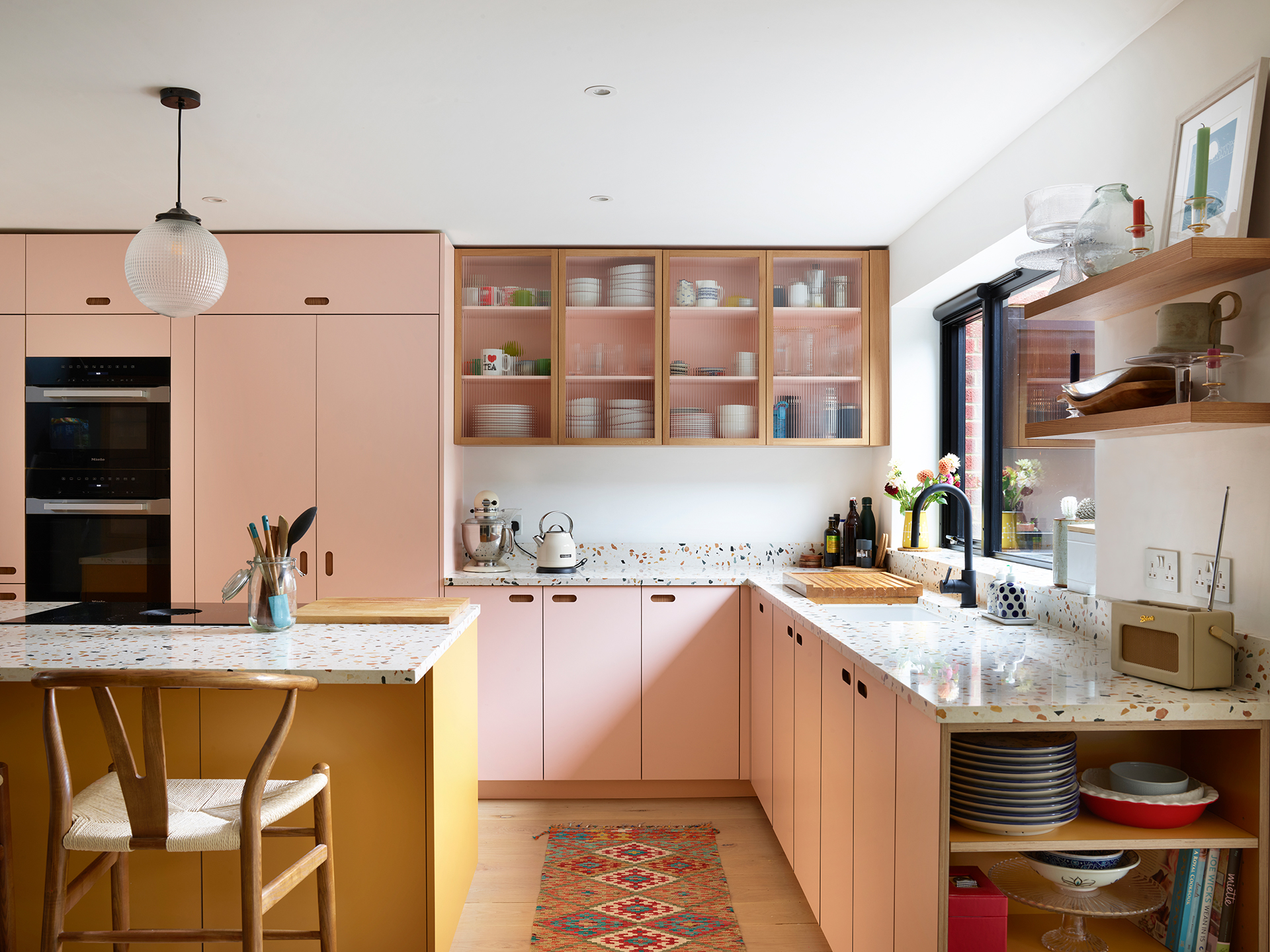 Colourful family kitchen in Hertfordshire including soft pink and mustard yellow Pluck cabinets, a large island and navy blue walls.