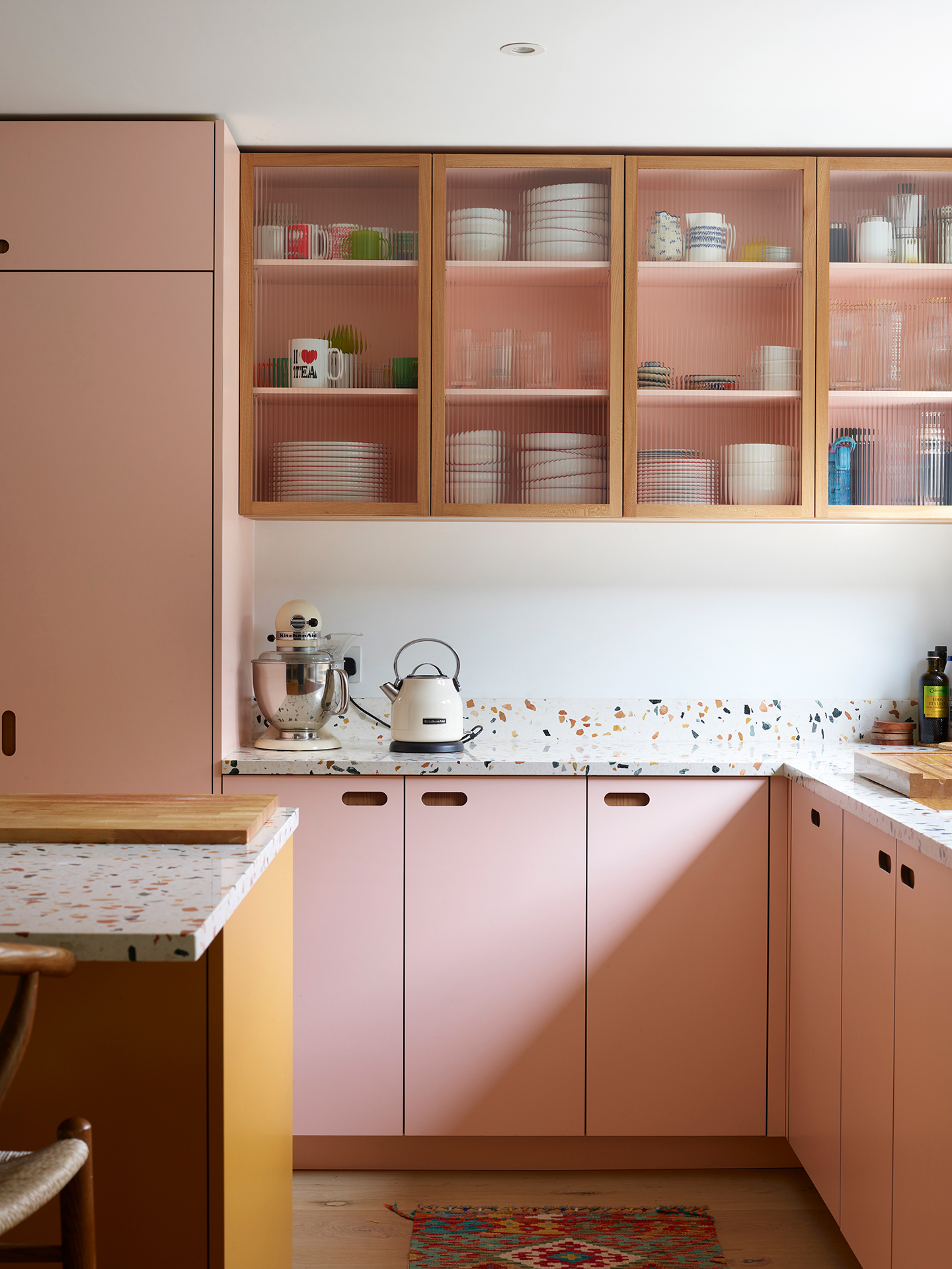 Colourful family kitchen in Hertfordshire including soft pink and mustard yellow Pluck cabinets, a large island and navy blue walls.