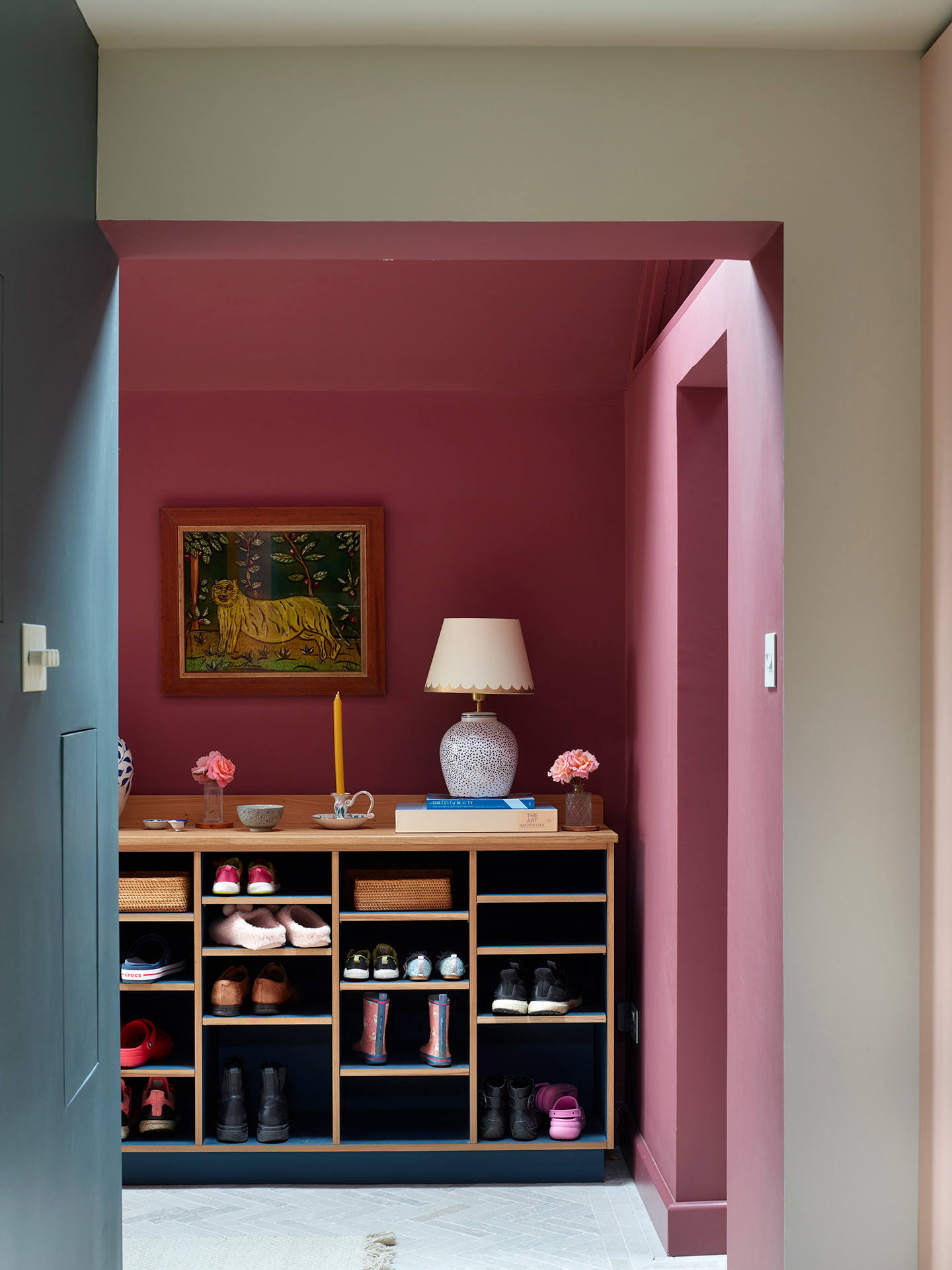 Entrance hall with raspberry hued walls, a navy sideboard and a framed painting hung behind.