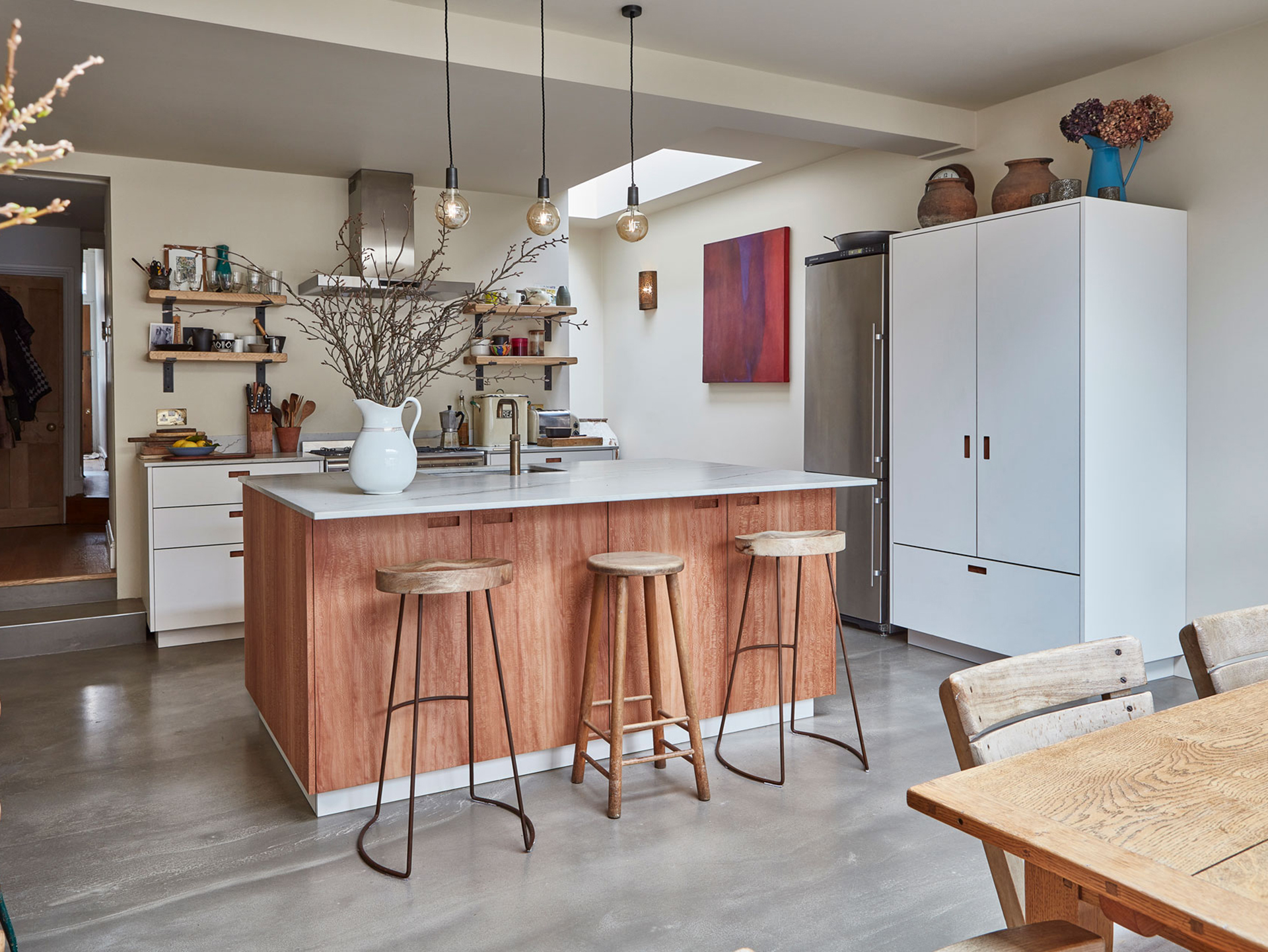 Open plan kitchen with neutral wood and white cabinetry topped with natural stone.