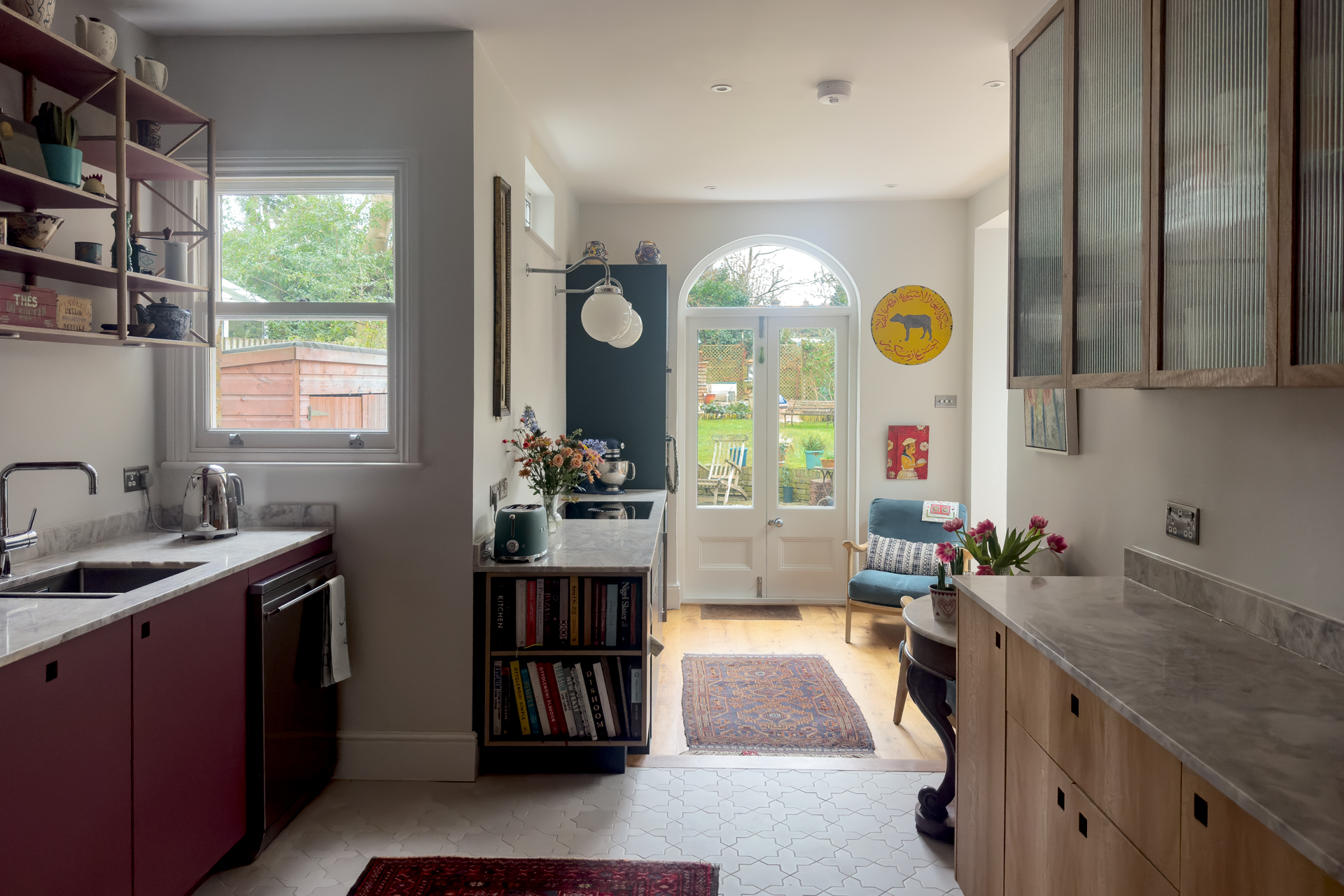 A cosy kitchen in Richmond London with pink and navy blue cabinets, stone worktops, vintage art and a wooden floor.