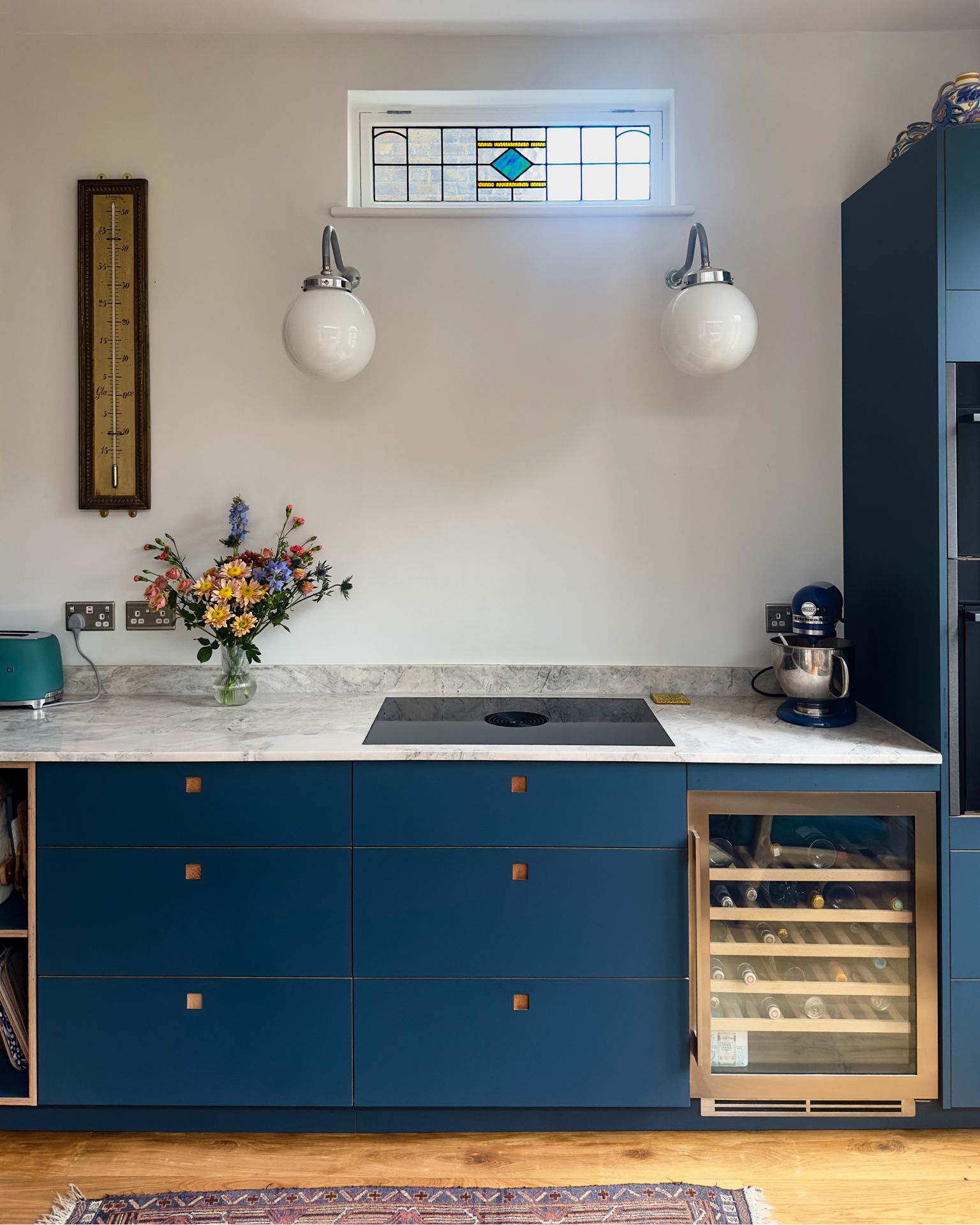 Long narrow kitchen with maroon and navy blue cabinets, open shelving and vintage artwork.