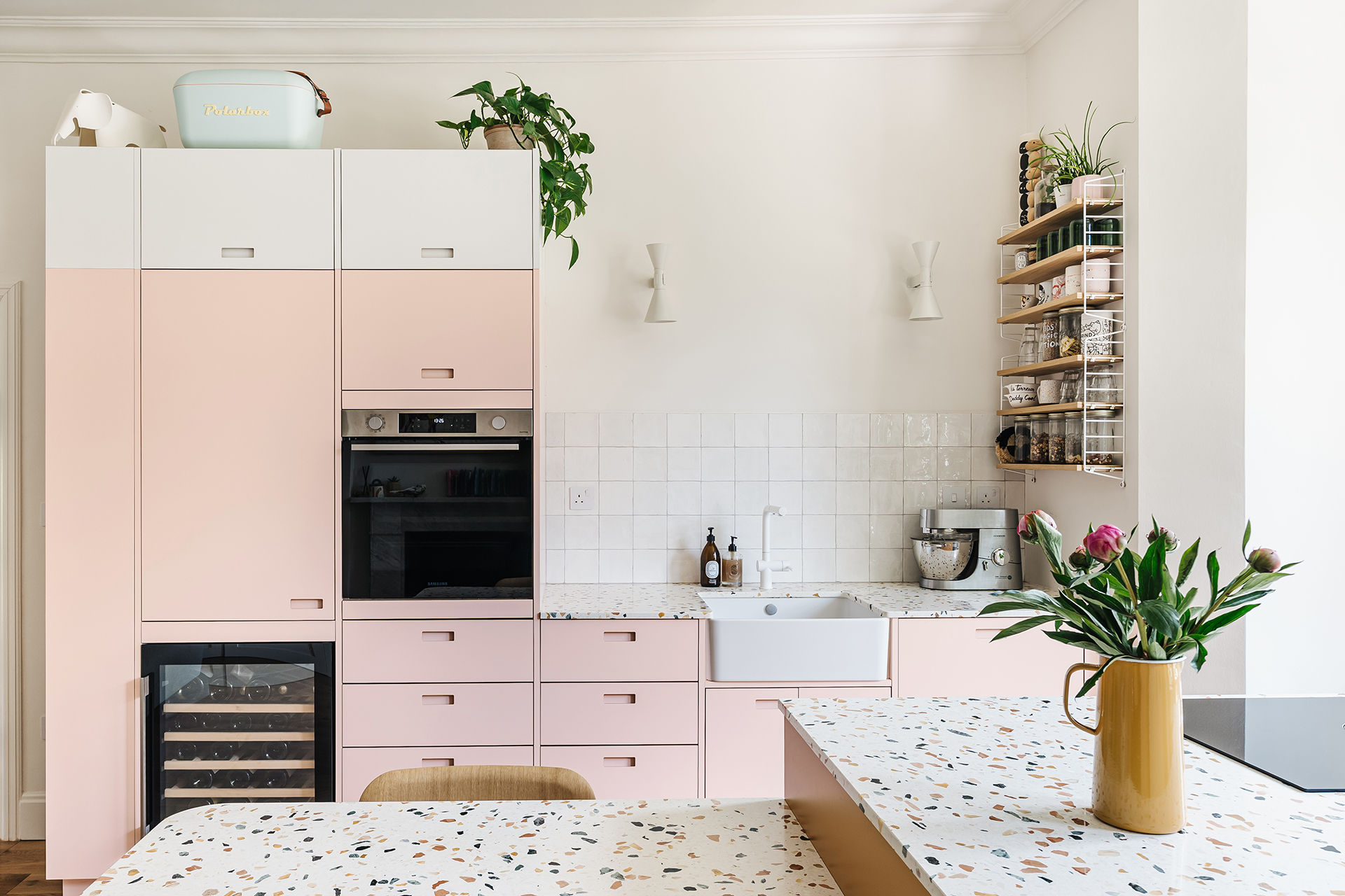 Bright Pluck kitchen with pastel pink cabinets, terrazzo worktops, and a dining table kitchen island combo in the centre.