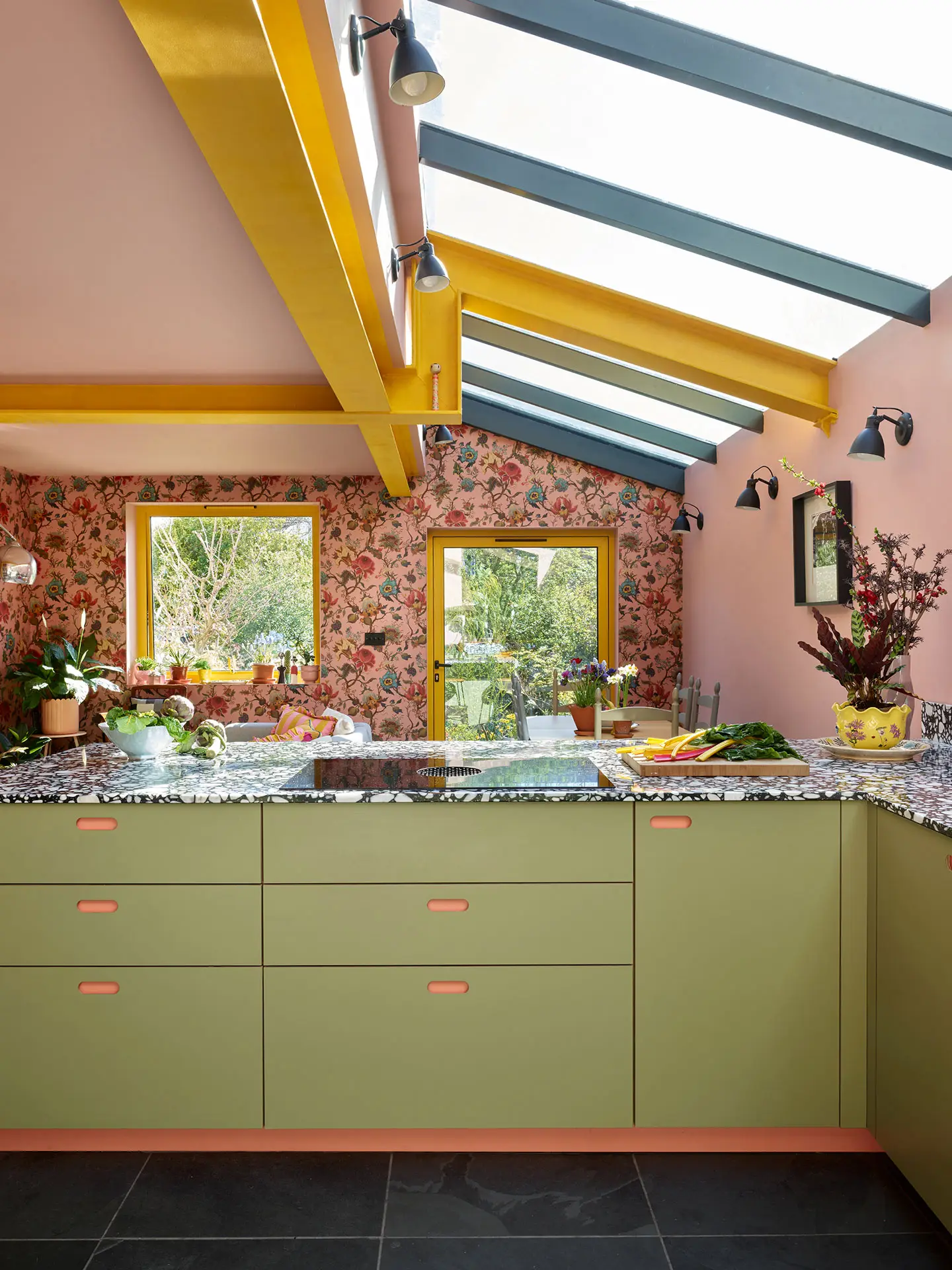 This colourful Pluck kitchen includes coral pink, soft pink and khaki green cabinetry, topped with black and white terrazzo.