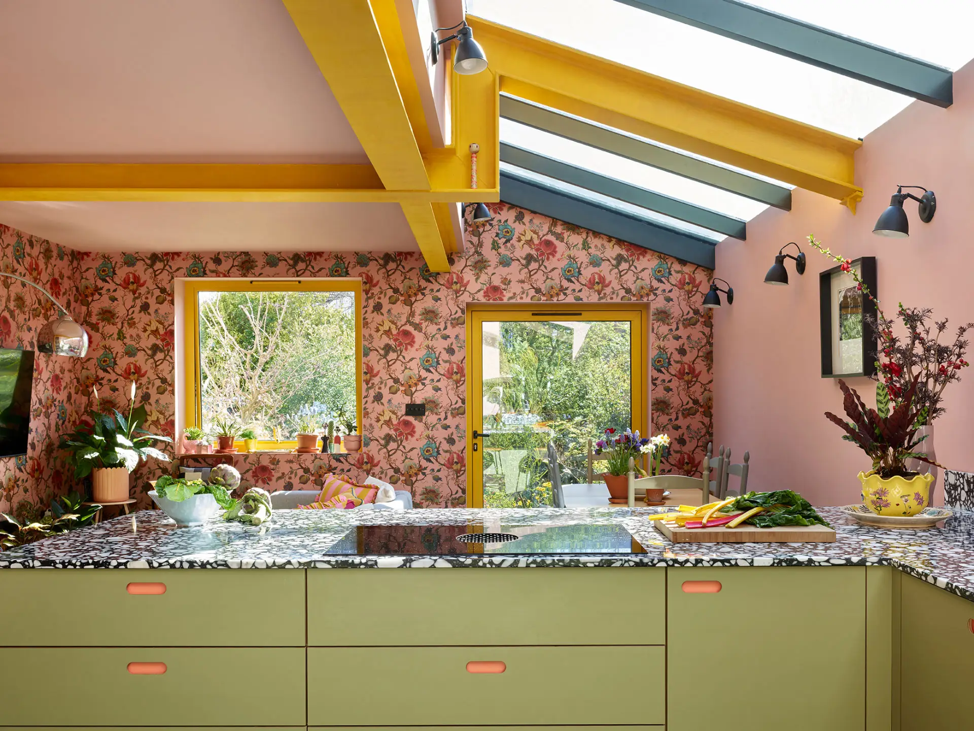This colourful Pluck kitchen includes coral pink, soft pink and khaki green cabinetry, topped with black and white terrazzo.