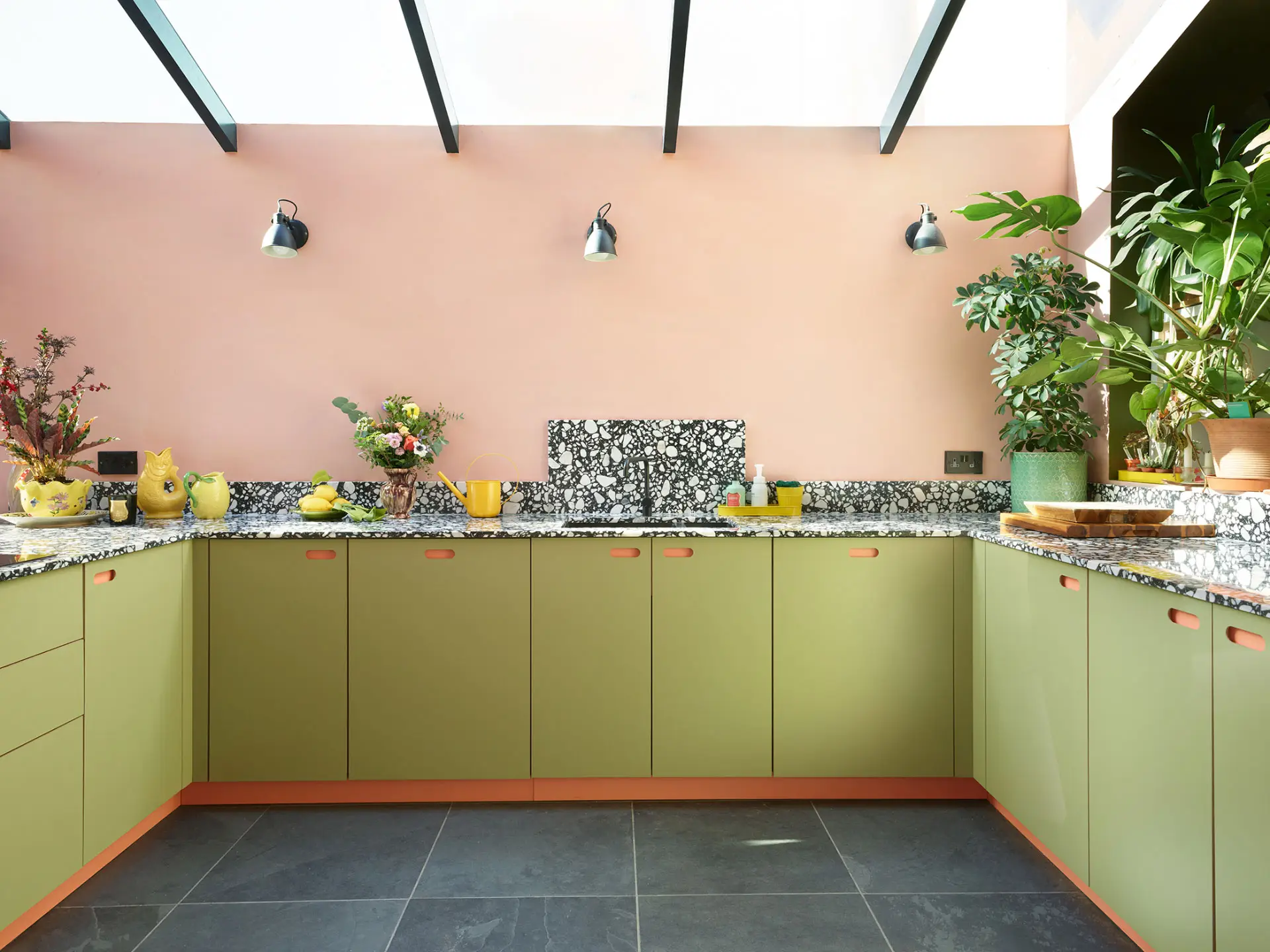 This colourful Pluck kitchen includes coral pink, soft pink and khaki green cabinetry, topped with black and white terrazzo.