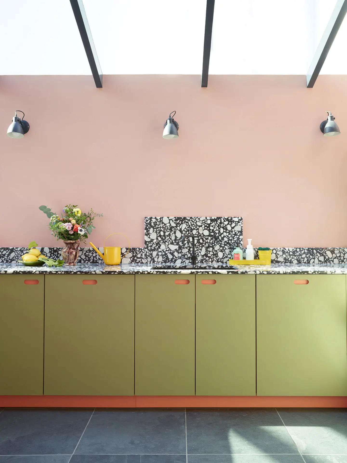 This colourful Pluck kitchen includes coral pink, soft pink and khaki green cabinetry, topped with black and white terrazzo.