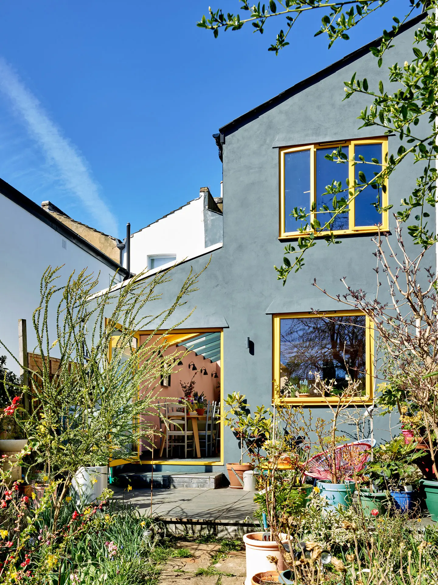 The exterior of a home with a colourful Pluck kitchen including coral pink, soft pink and khaki green cabinetry, topped with black and white terrazzo.