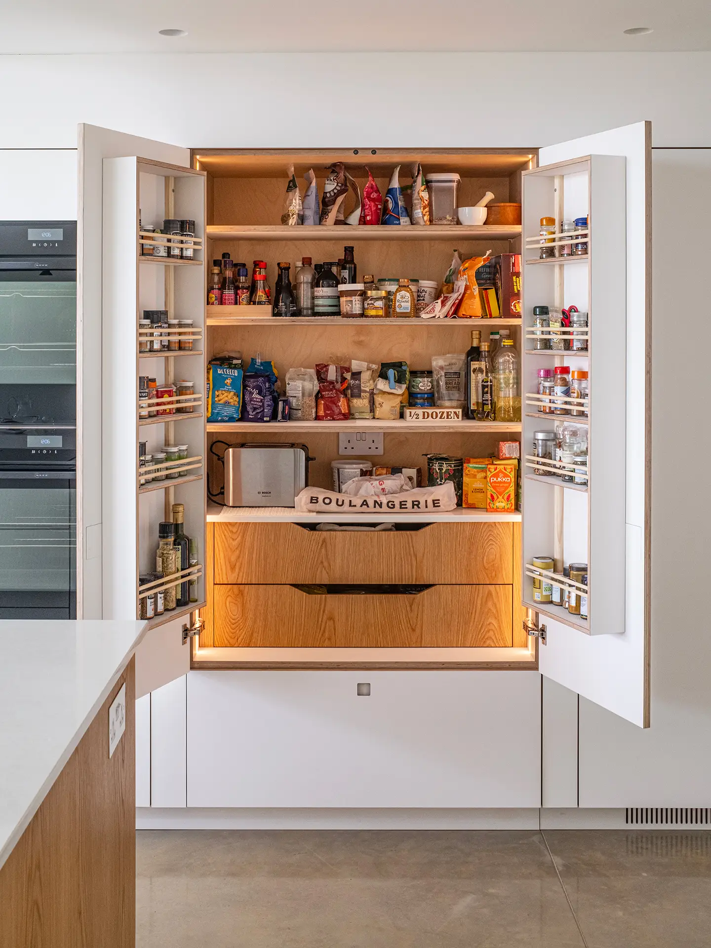 Pluck pantry cupboard with it's door open revealing lights, shelves and drawers.
