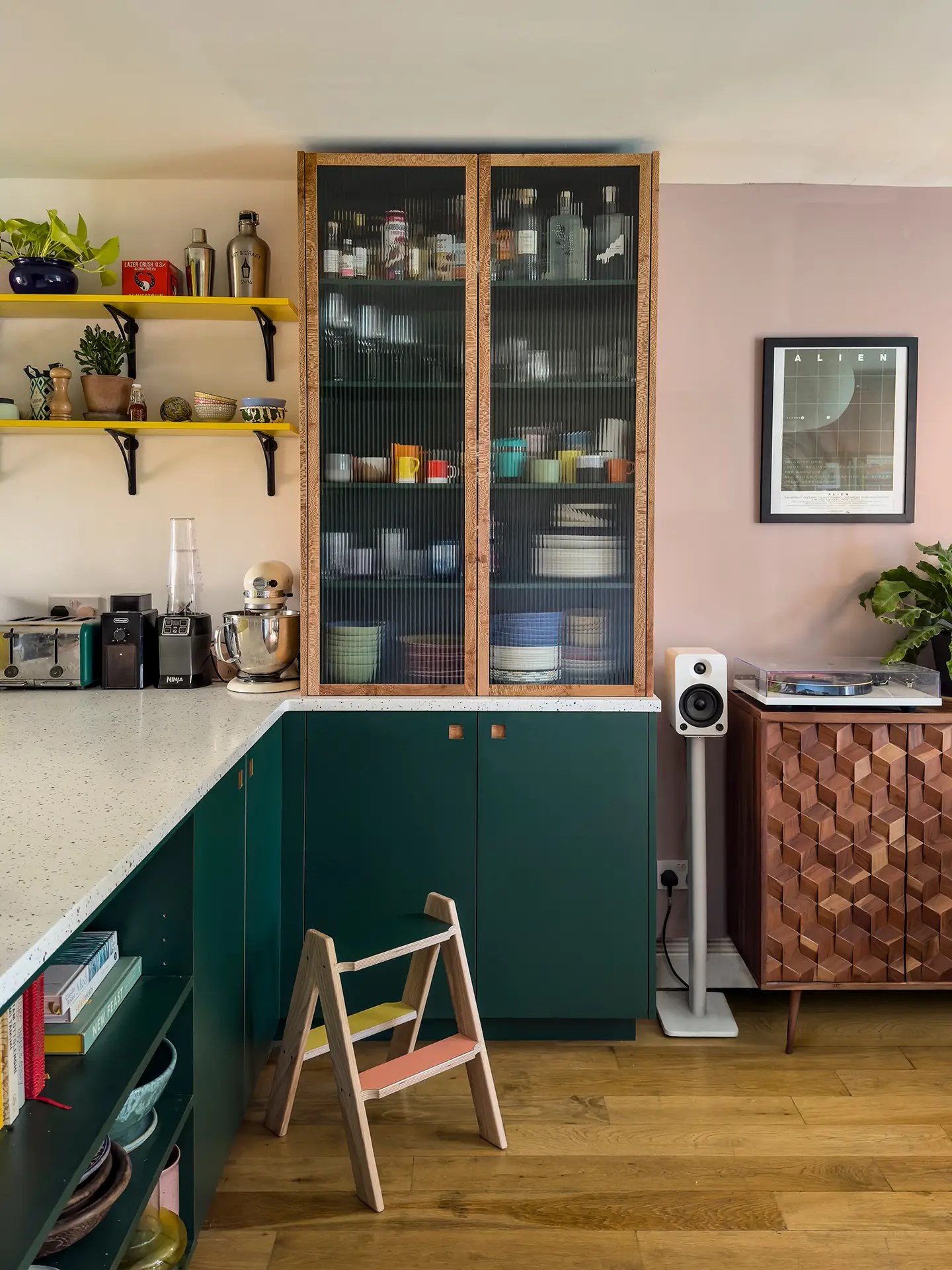 A green Pluck kitchen with tall glass cabinets used to store glassware and bottles.