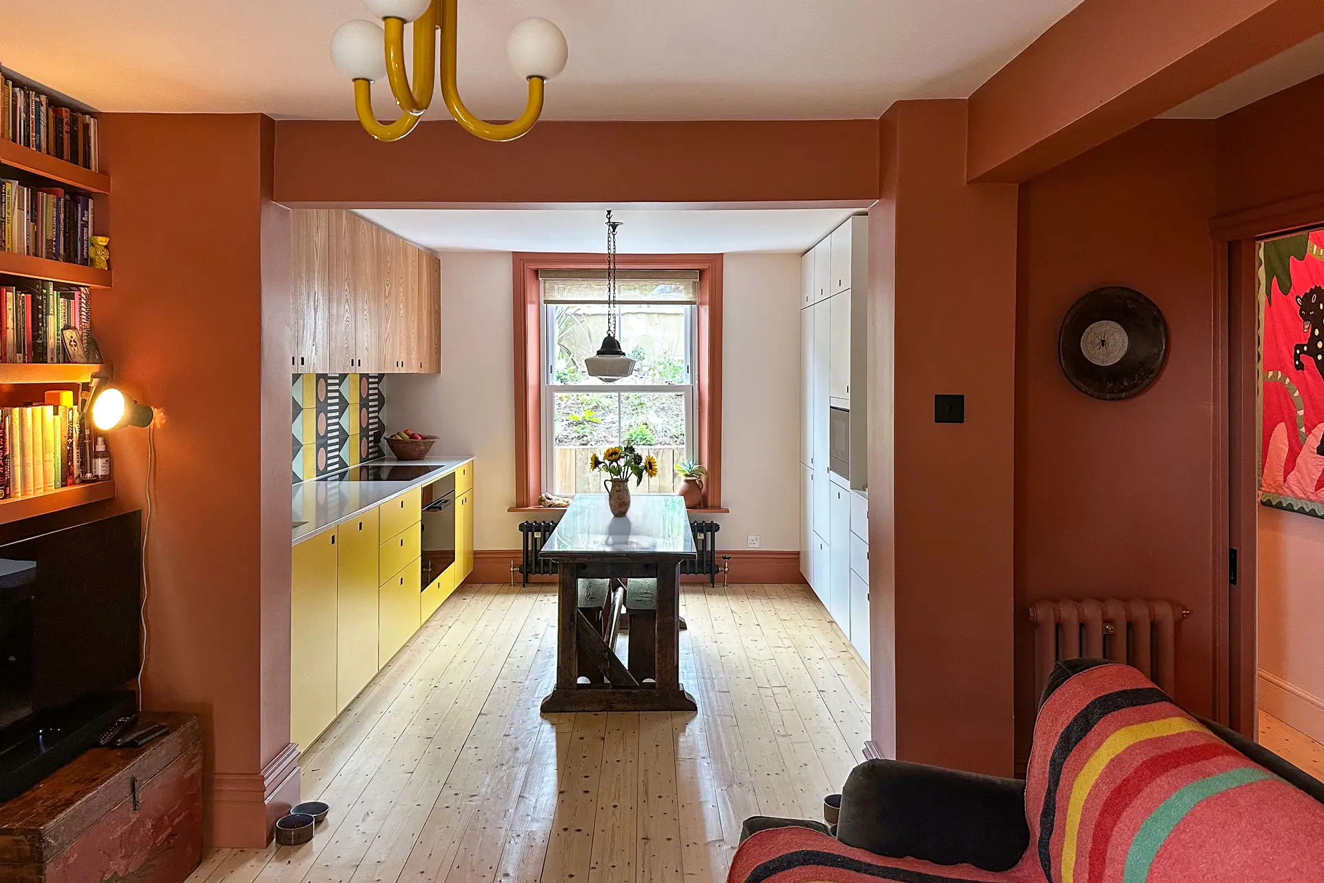A family kitchen in Greenwich with colourful cabinetry, wooden floors, patterned tiles and antique table.