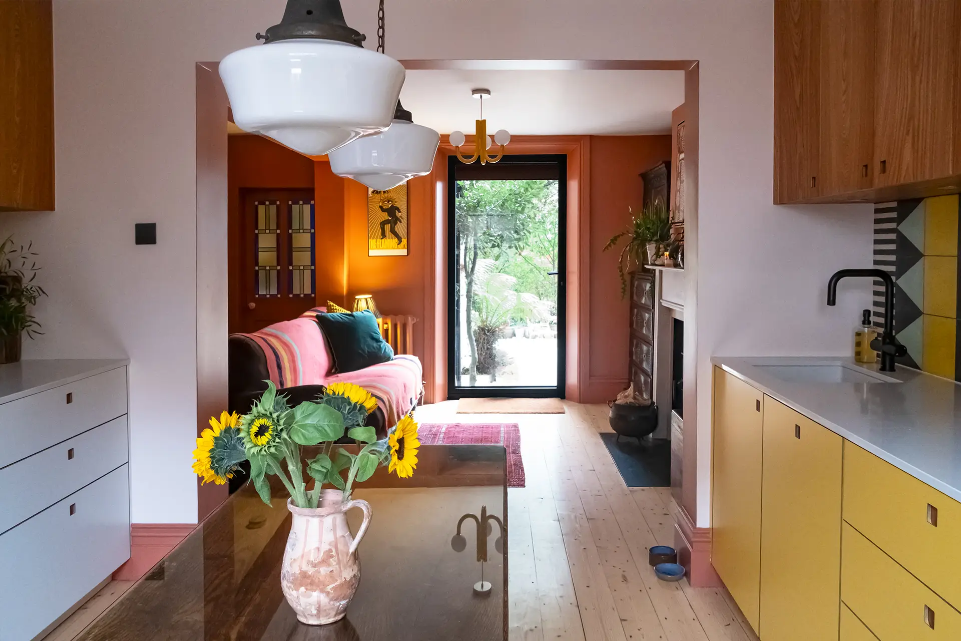 A galley kitchen in a London family home with white, wood, and yellow Pluck cabinetry and colourful tiles.