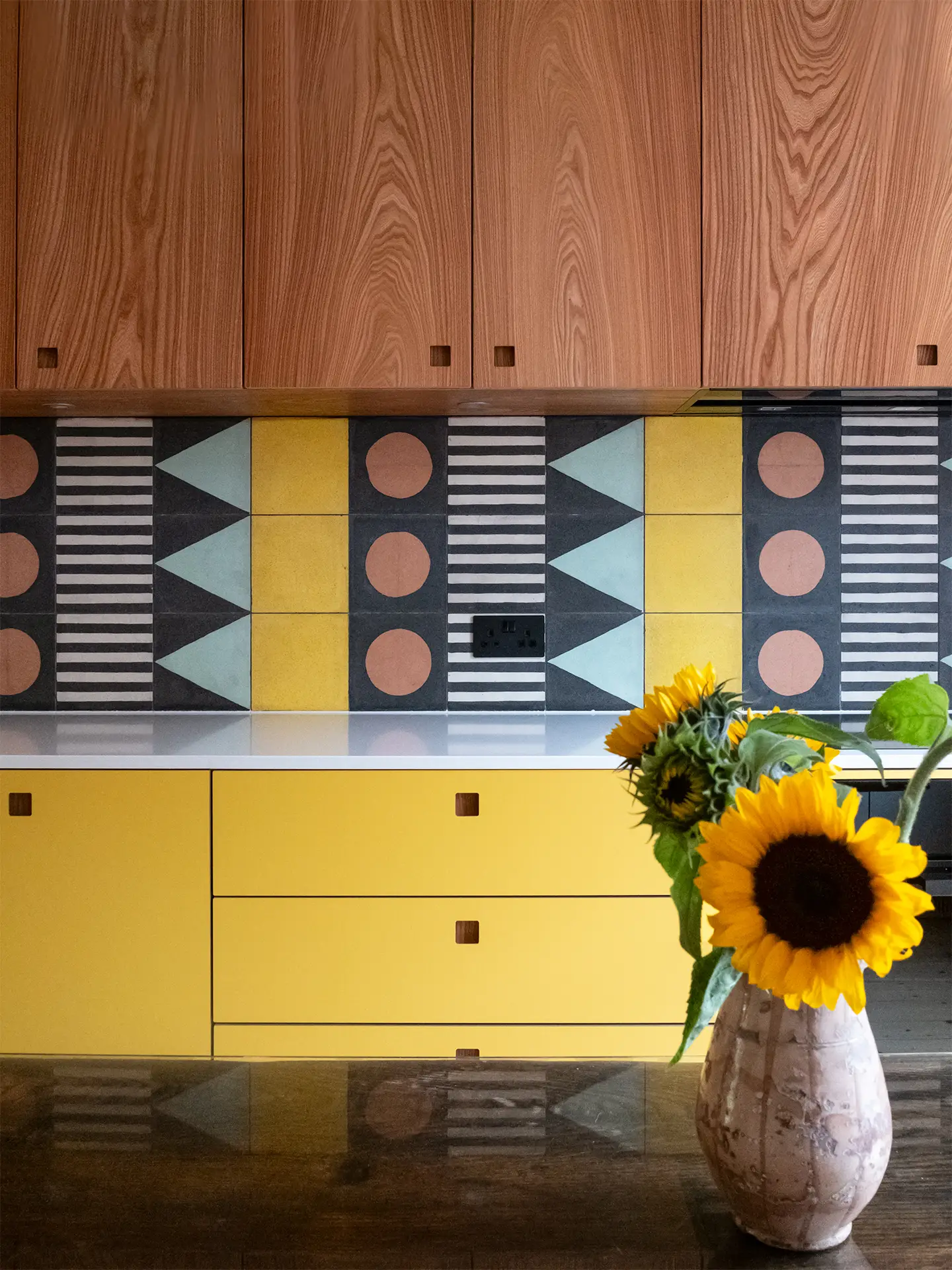 A family kitchen in Greenwich with colourful cabinetry, wooden floors, patterned tiles and antique table.