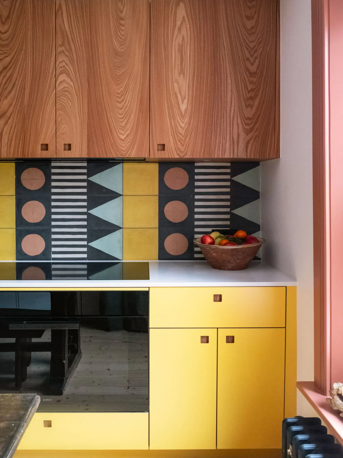 A galley kitchen in a London family home with white, wood, and yellow Pluck cabinetry and colourful tiles.