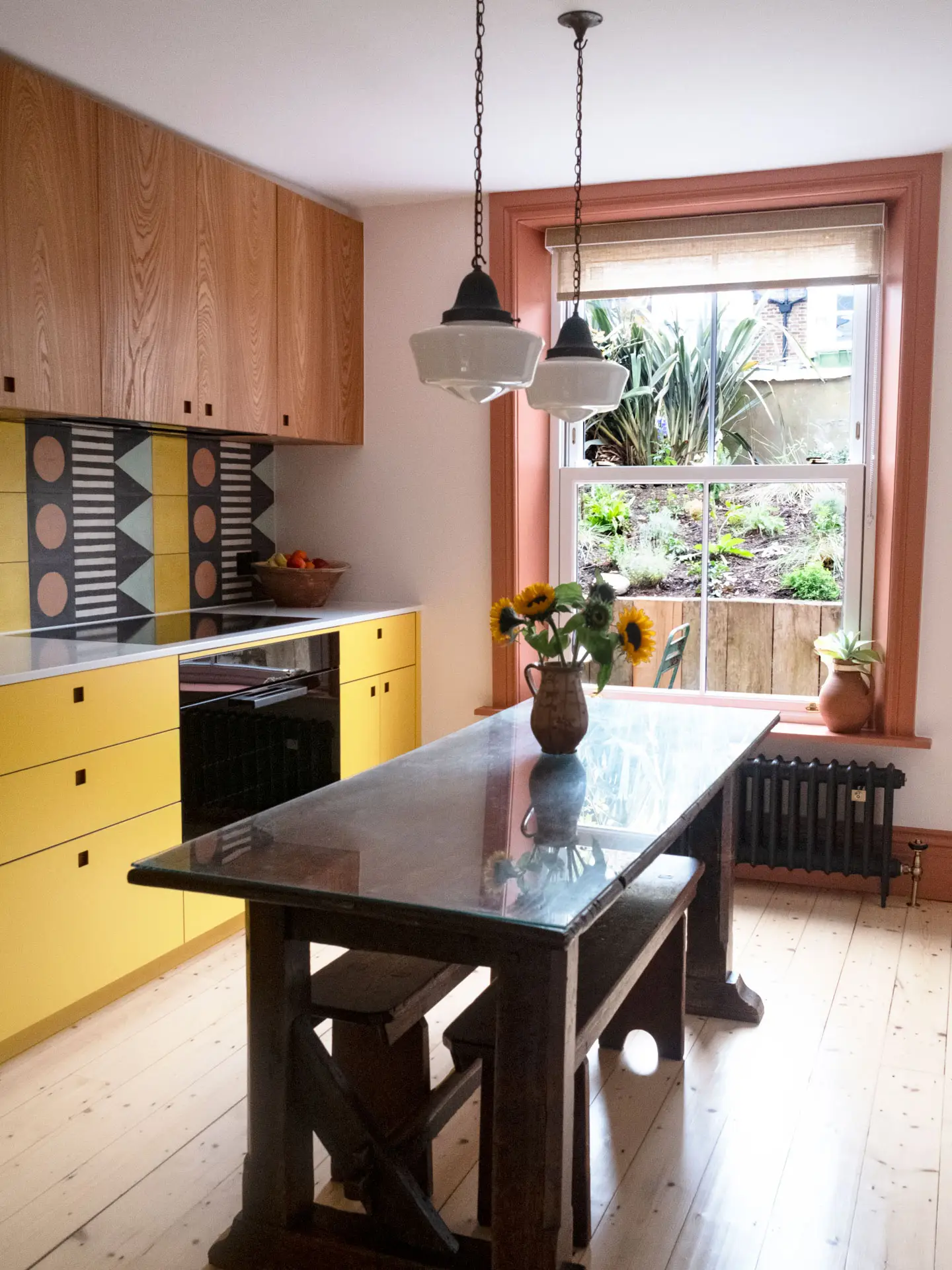 A galley kitchen in a London family home with white, wood, and yellow Pluck cabinetry and colourful tiles.