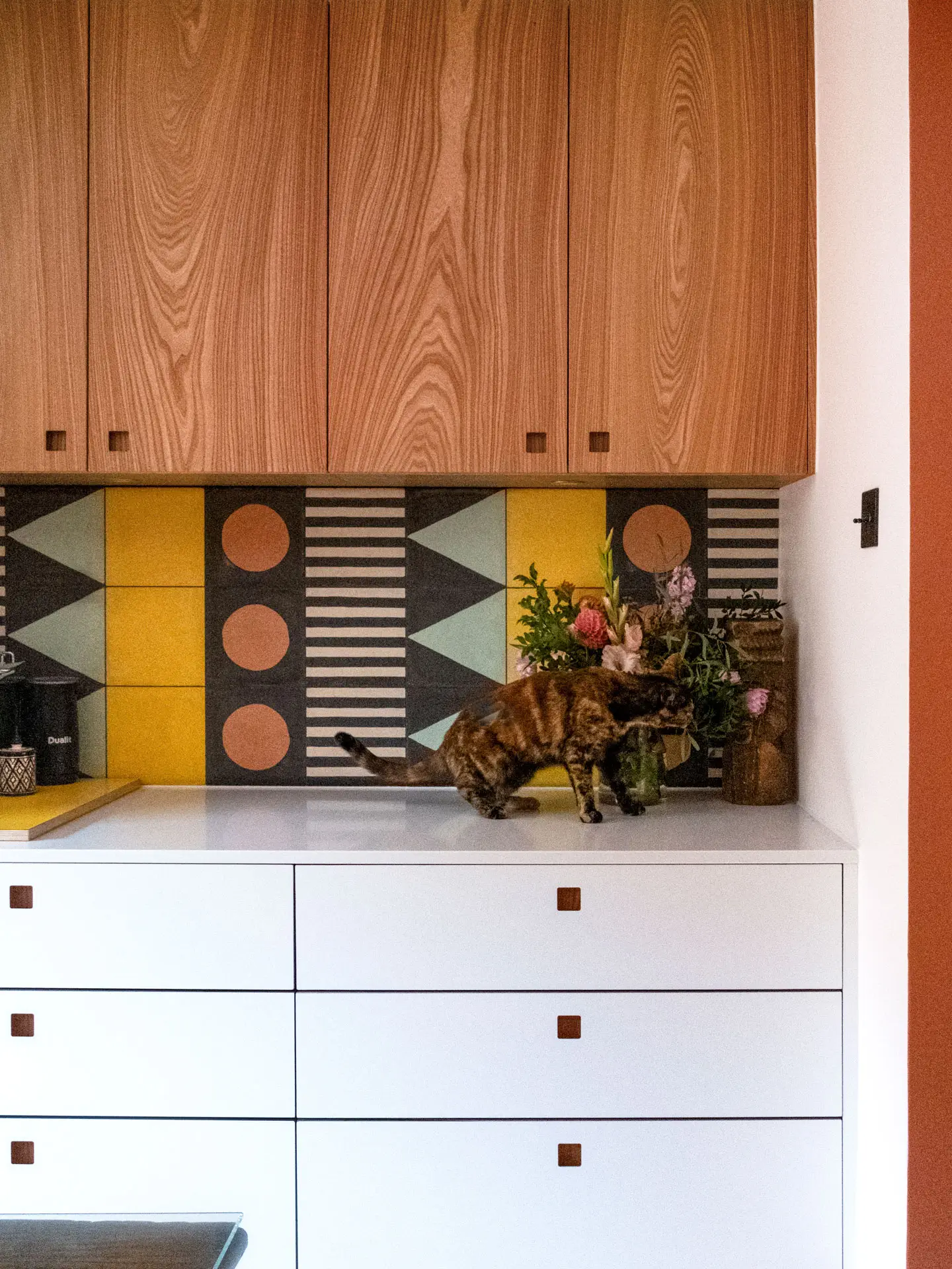 A family kitchen in Greenwich with colourful cabinetry, wooden floors, patterned tiles and antique table.