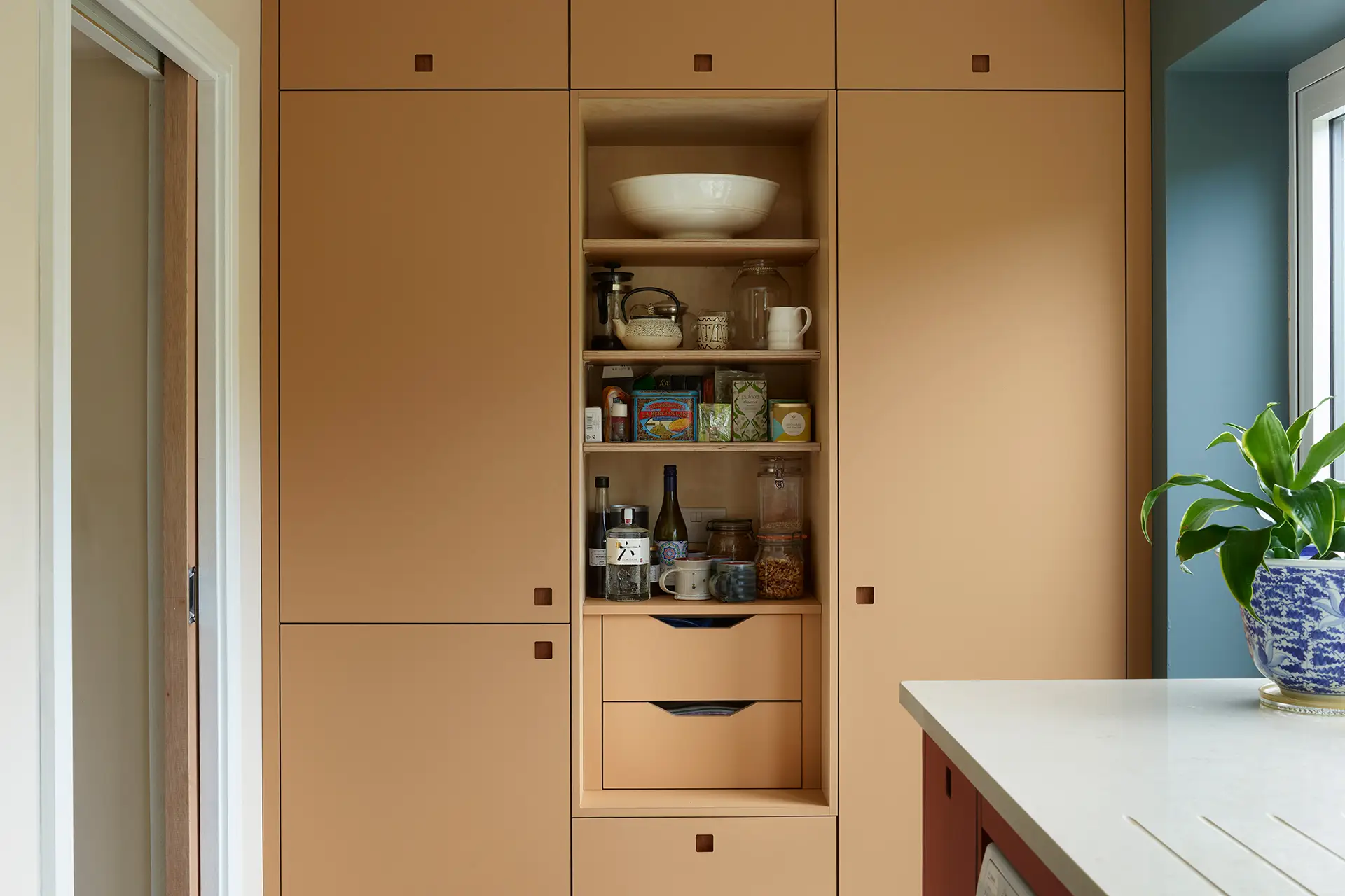 Moody hues of a kitchen in Essex with orange and red two tone cabinetry and a navy blue wall.