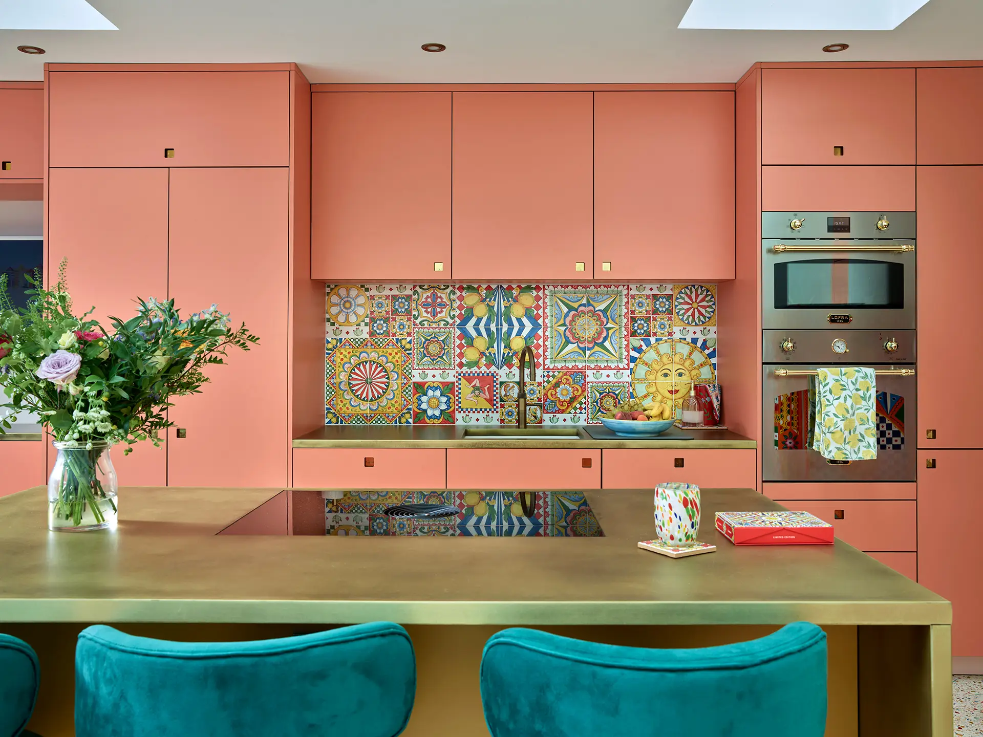 Coral Pink Kitchen cabinetry with brass worktops, a large kitchen island and bright tiled backsplash.