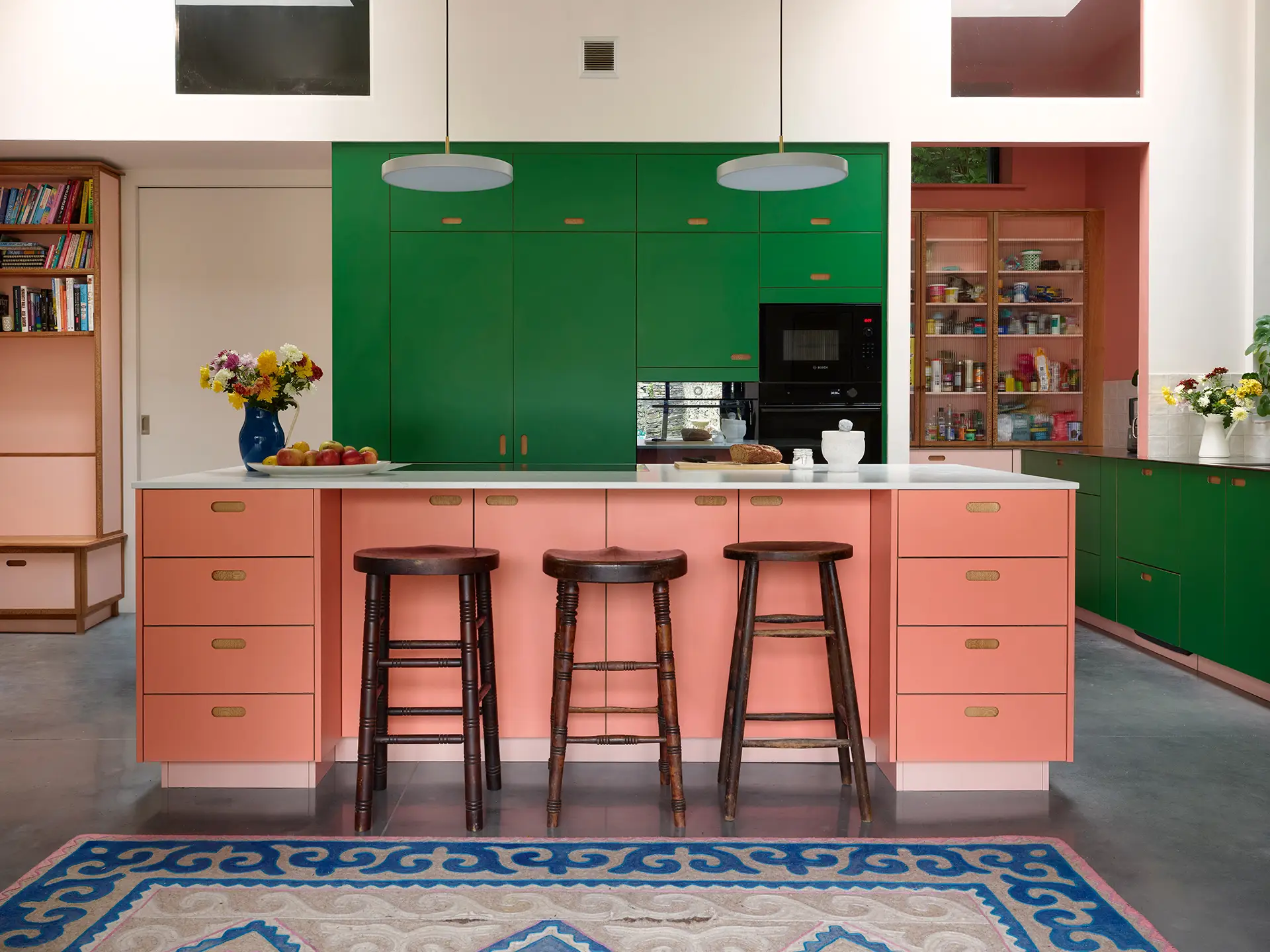A pink and green pluck kitchen in rural wales with a large island and a small table with banquette seating.