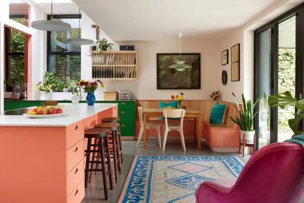 A pink and green pluck kitchen in rural wales with a large island and a small table with banquette seating.