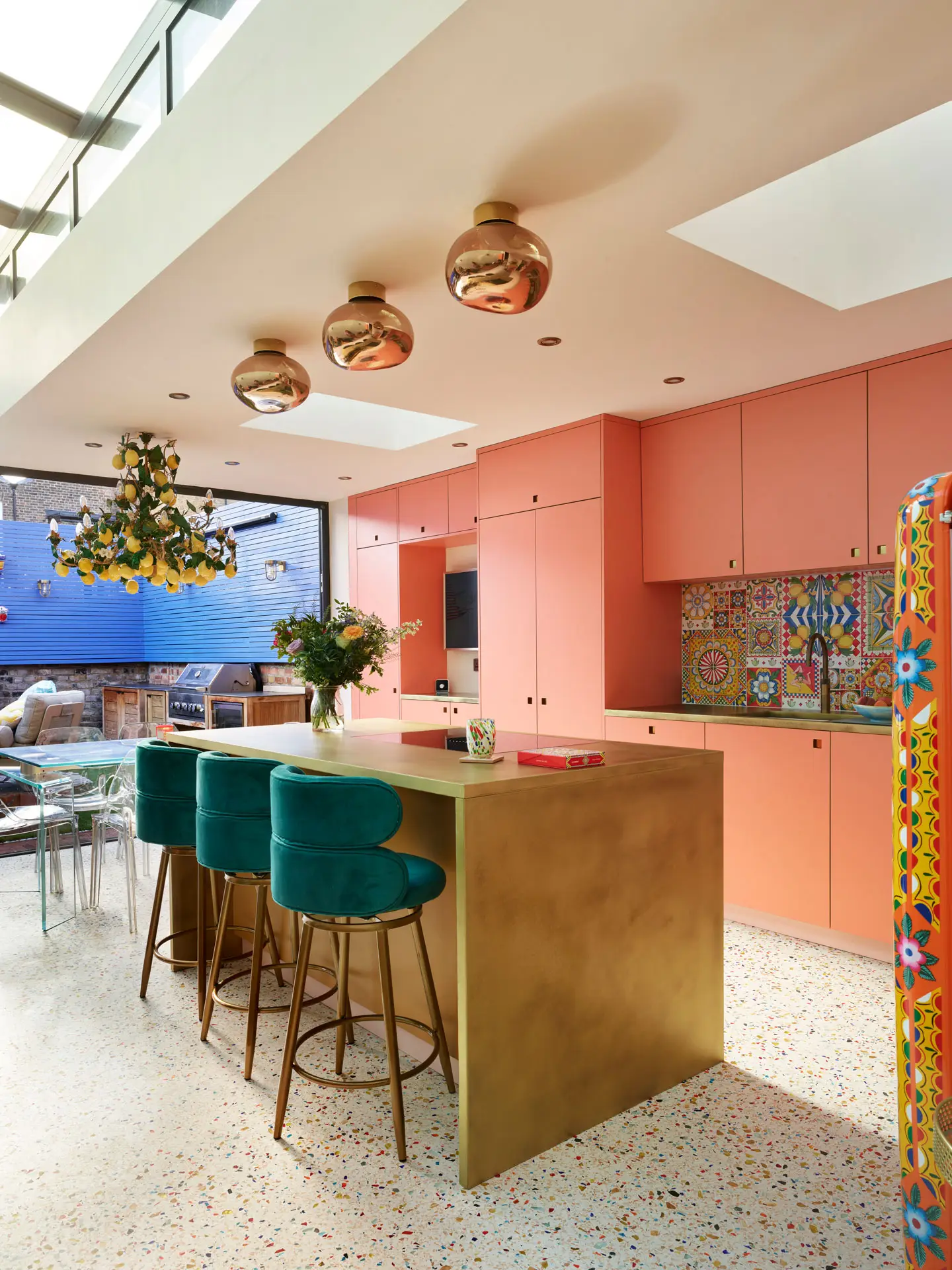 A coral pink Pluck kitchen with colourful terrazzo flooring, brass worktops and an Italian lemon chandelier.
