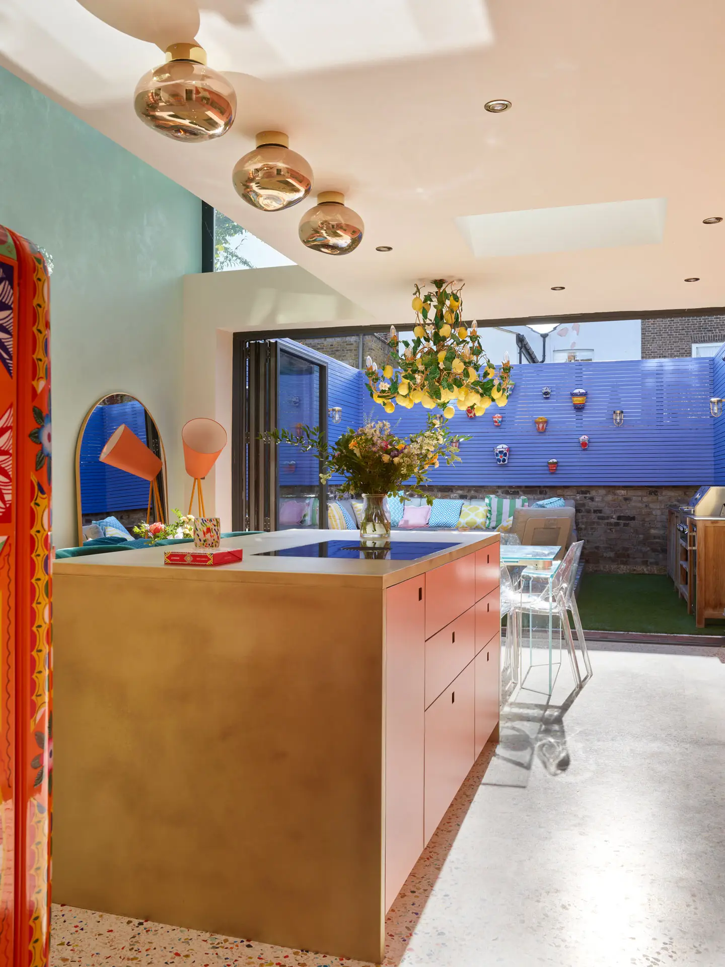 A coral pink Pluck kitchen with colourful terrazzo flooring, brass worktops and an Italian lemon chandelier.