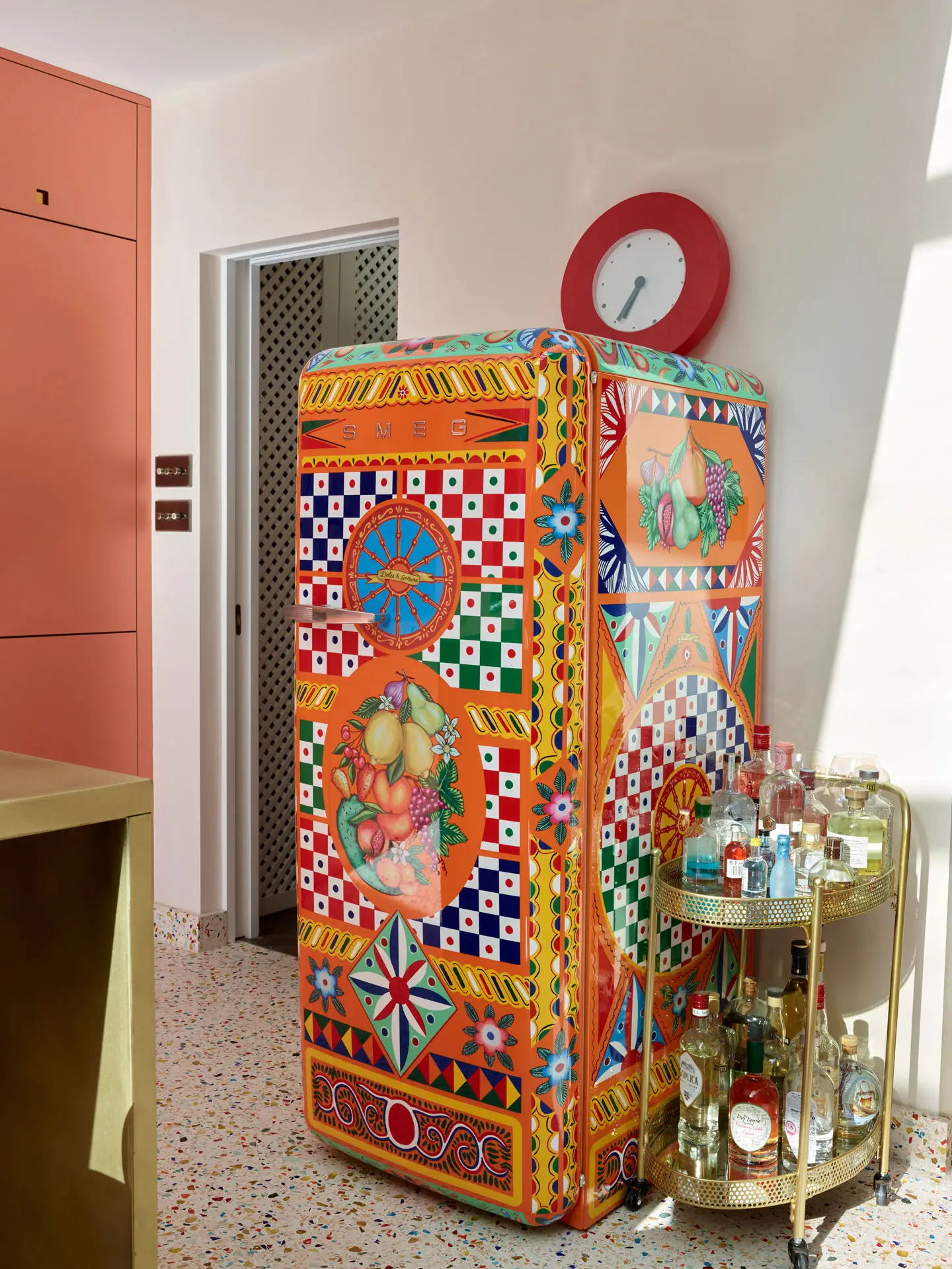 A Dolce & Gabbana Smeg fridge in a coral pink Pluck kitchen with colourful terrazzo flooring.