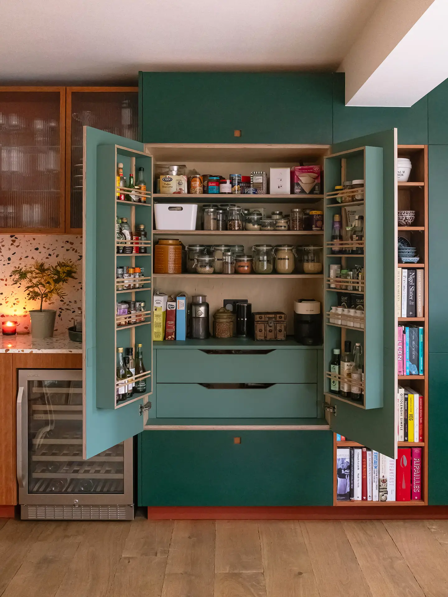 A large green Pluck larder cabinet with its doors open to reveal internal shelving.