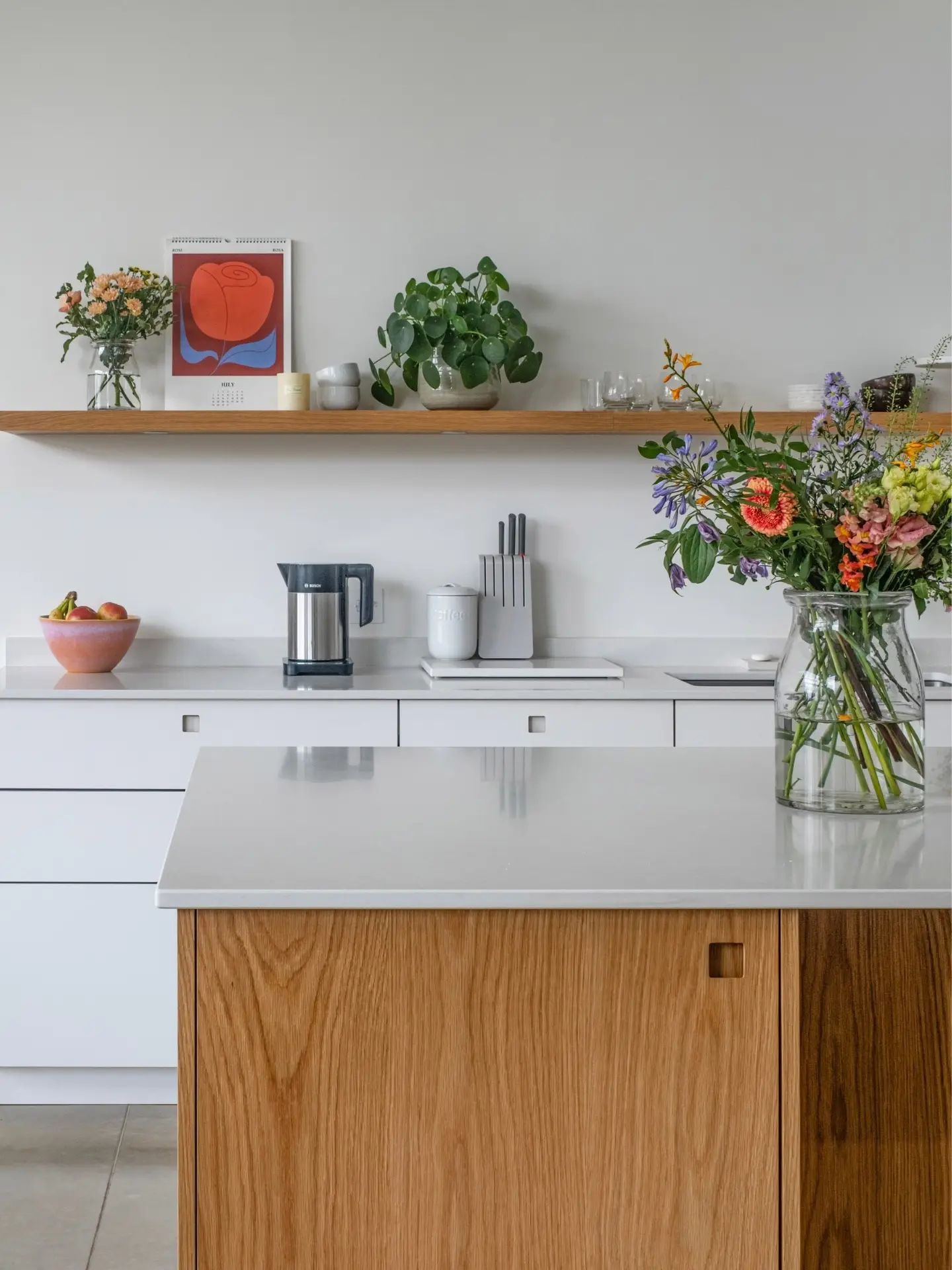 Minimalist kitchen with white cabinetry, an oak island and a floating oak shelf on the wall.