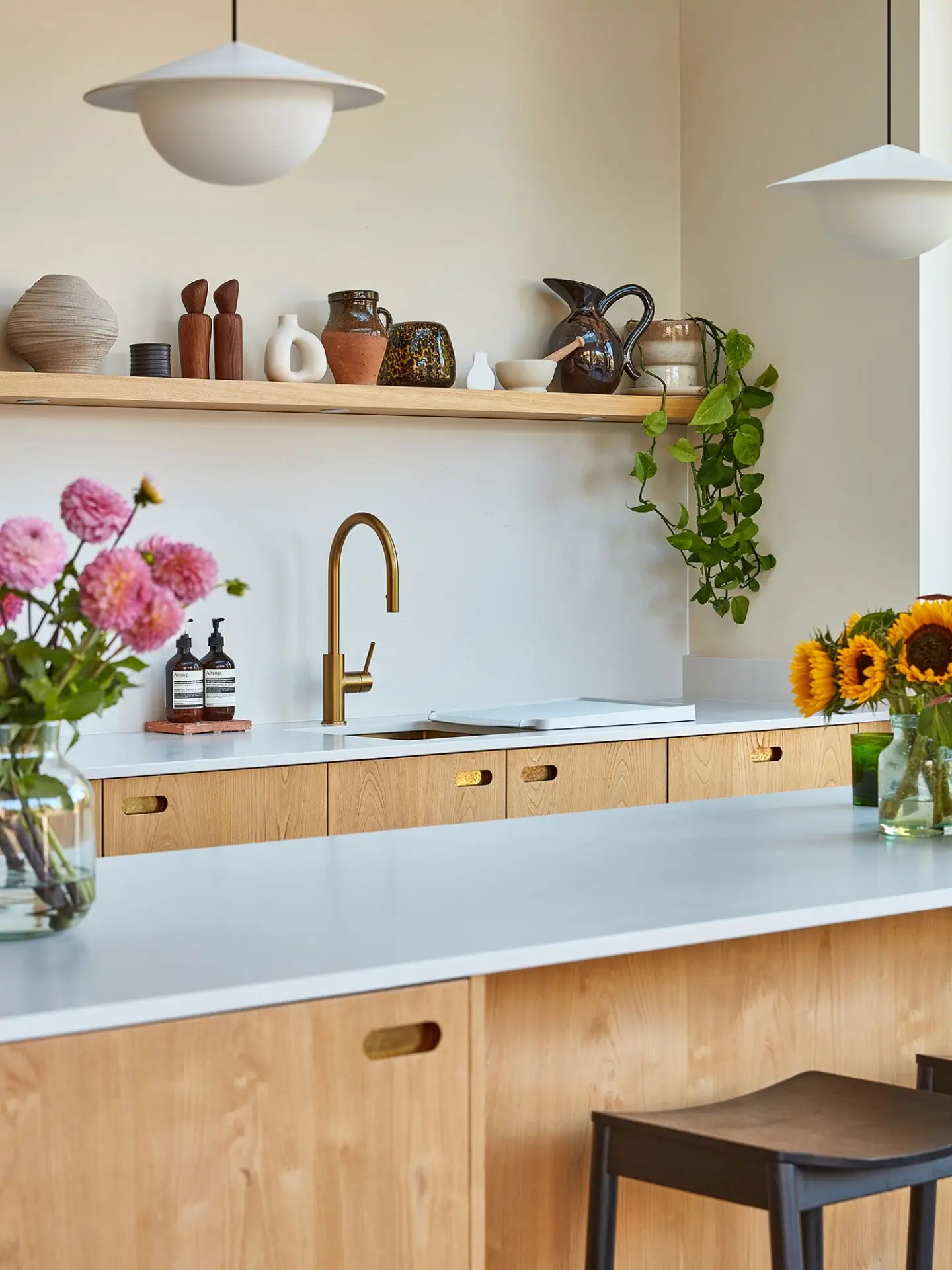 Minimalist kitchen with light wood cabinets and off white worktops. Shelves display pottery and plants.