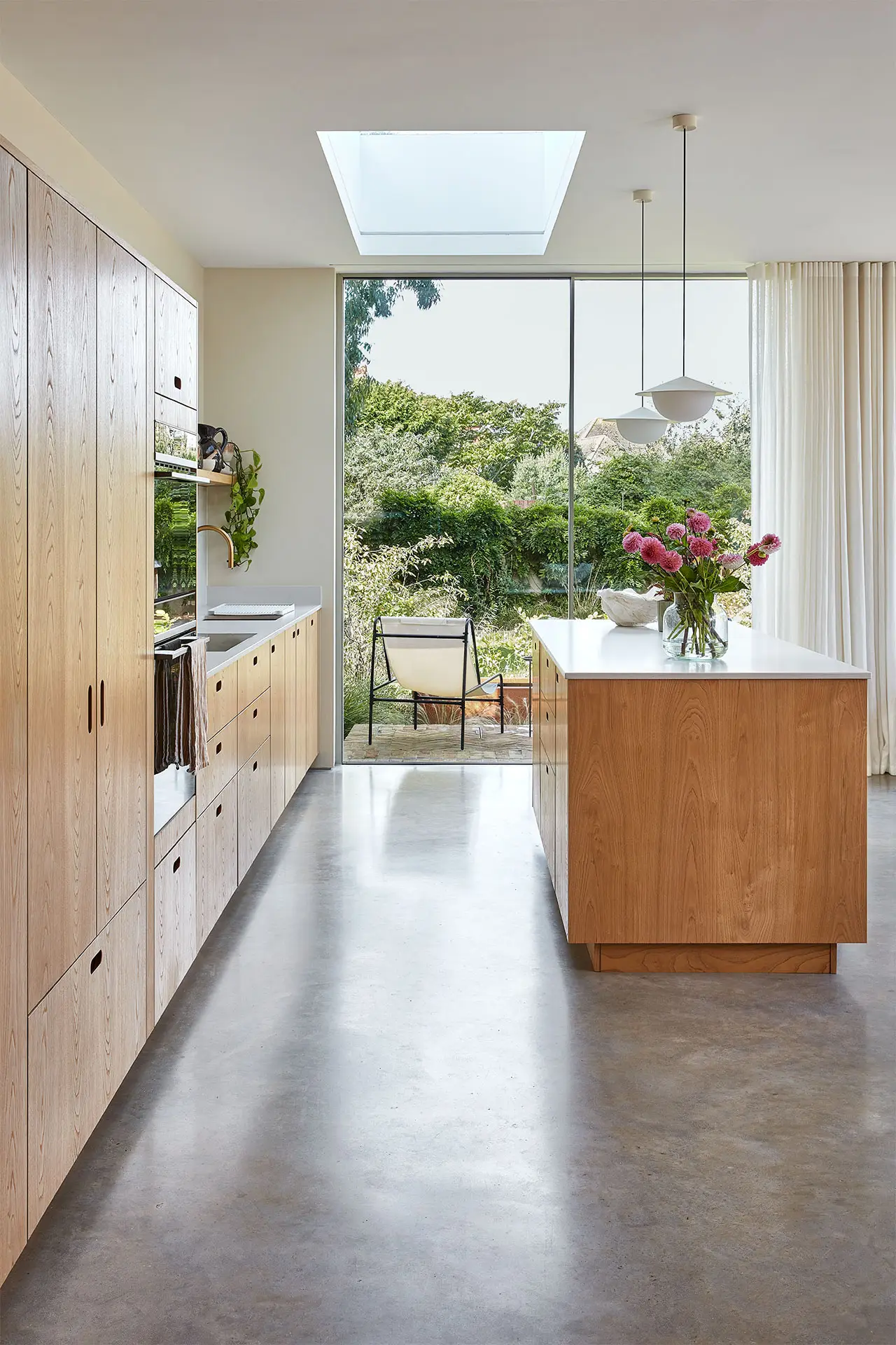 Pluck-Journal-The-Scandi-Chic-Kitchen-7 A kitchen in a family home in Brighton with wood cabinetry and brass handles, including an island, larder and shelf and grey concrete floor.