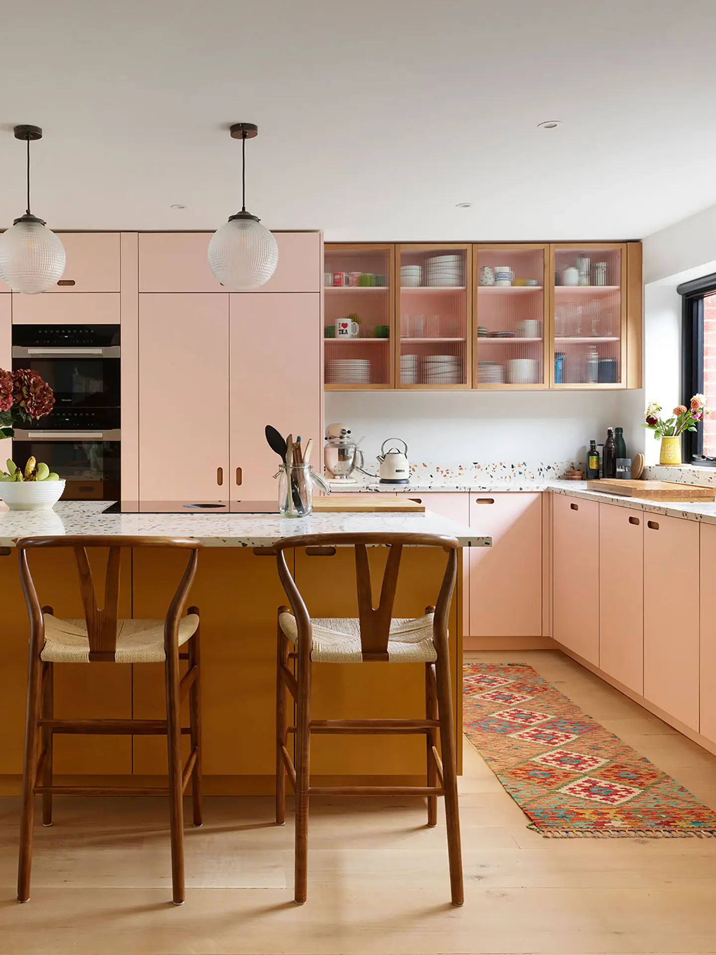 Colourful family kitchen in Hertfordshire including soft pink and mustard yellow Pluck cabinets, a large island and navy blue walls.