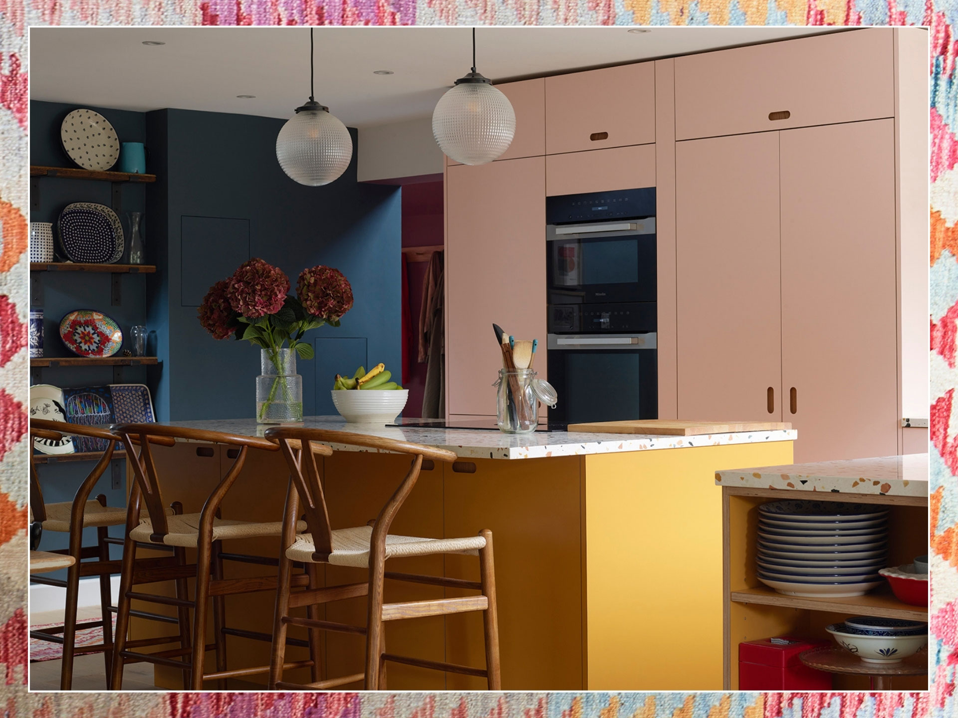 Colourful family kitchen in Hertfordshire including soft pink and mustard yellow Pluck cabinets, a large island and navy blue walls.