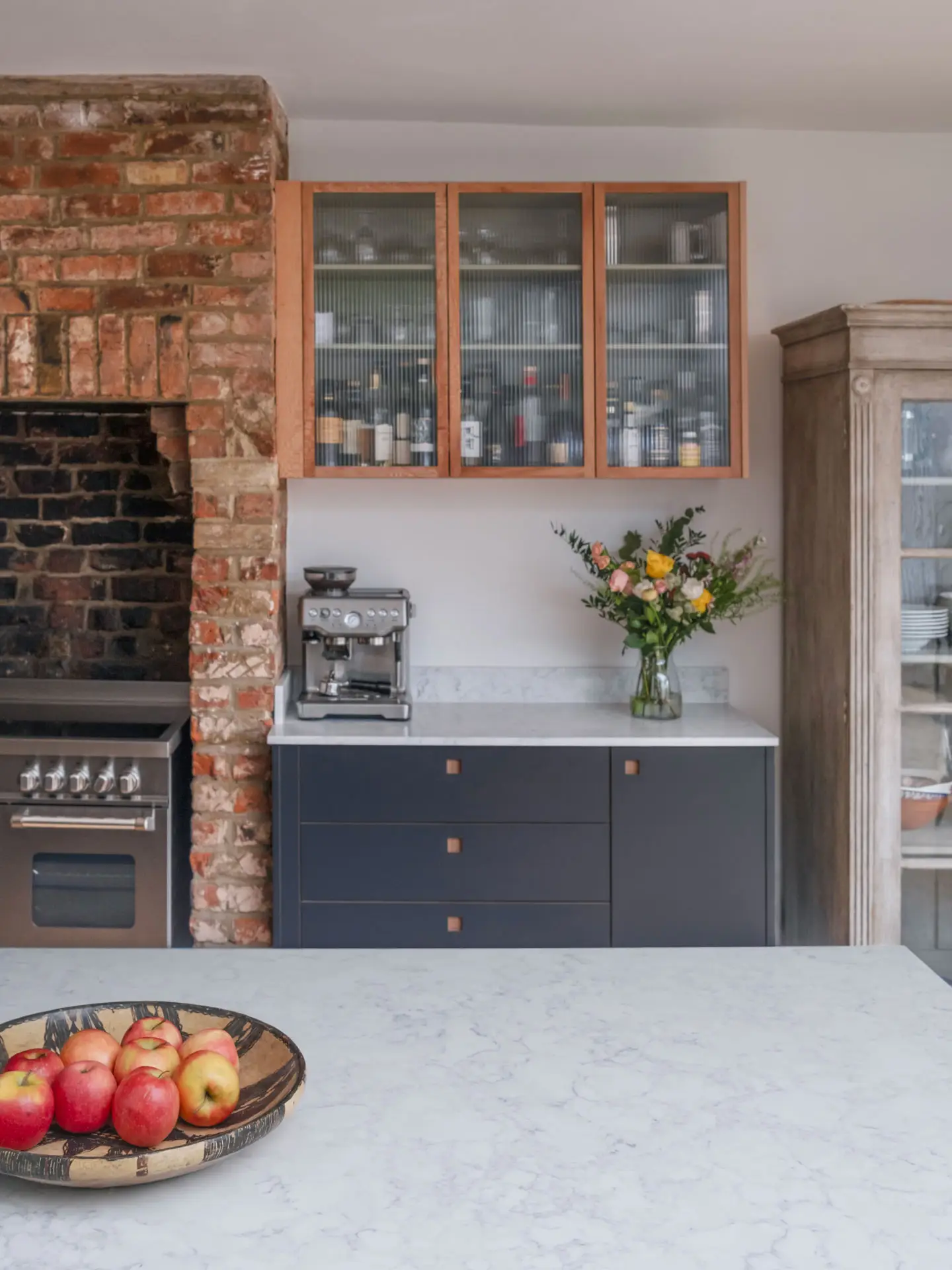 Cool hues in an open plan Pluck kitchen including a larder, shelving and glass cabinet.