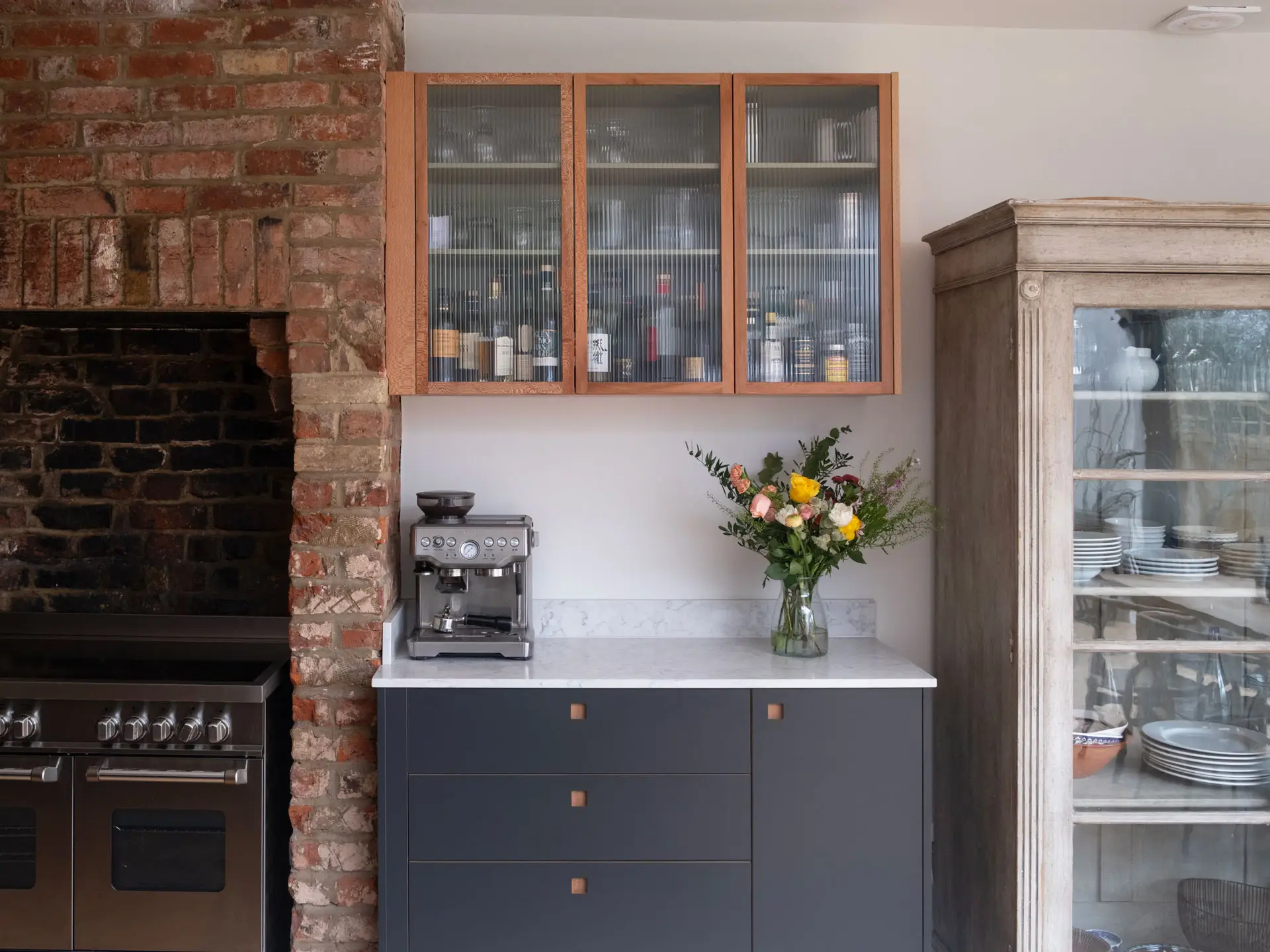 Cool hues in an open plan Pluck kitchen including a larder, shelving and glass cabinet.