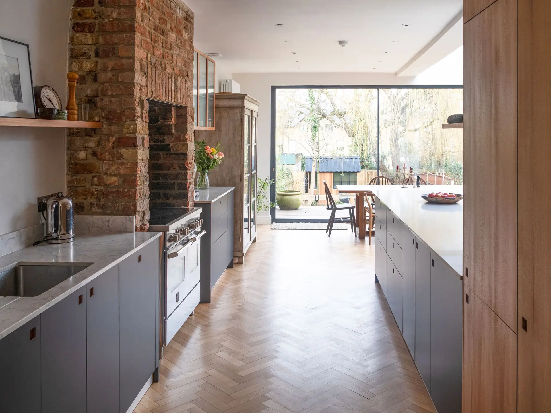Cool hues in an open plan Pluck kitchen including a larder, shelving and glass cabinet.