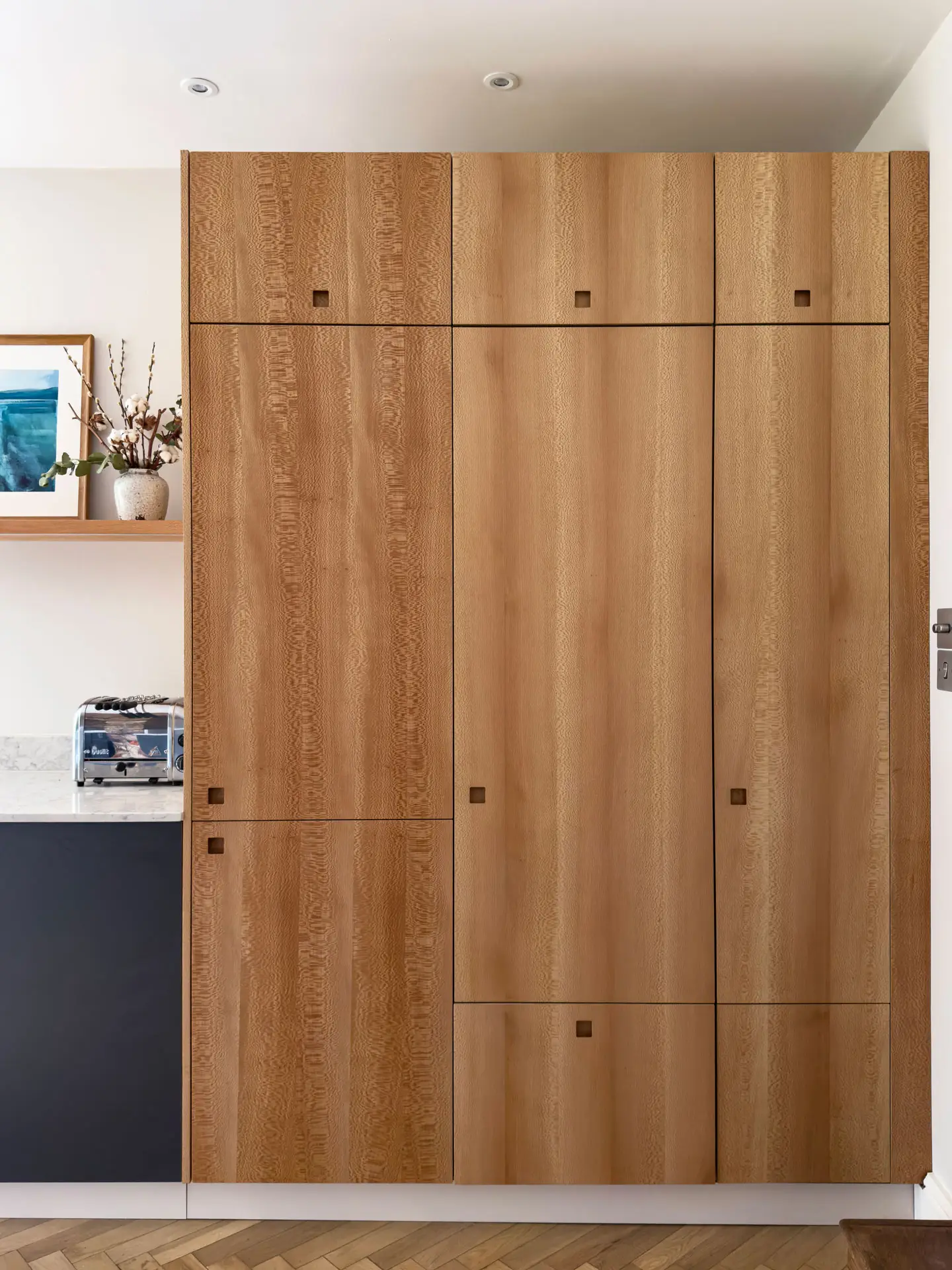 Cool hues in an open plan Pluck kitchen including a larder, shelving and glass cabinet.